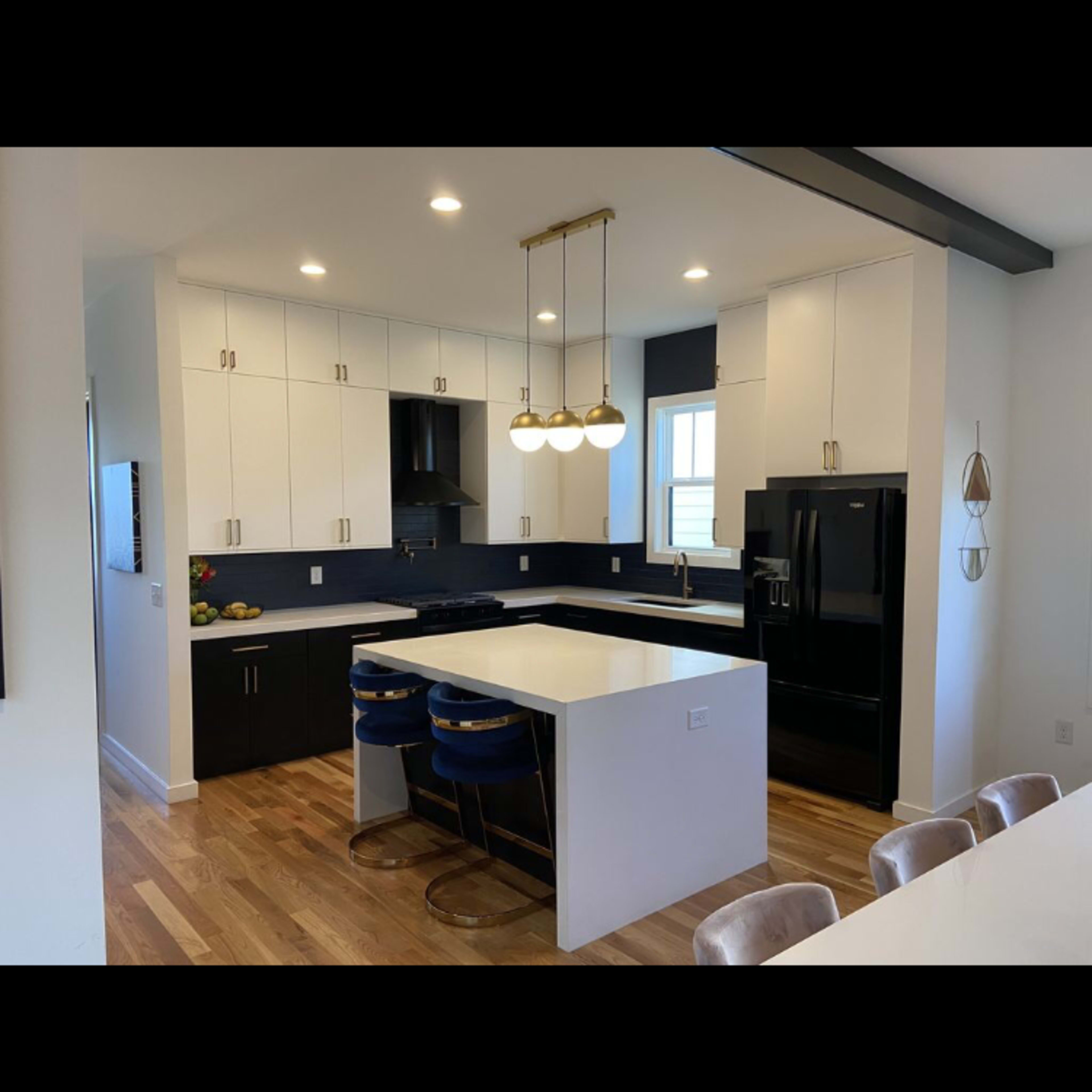 A modern kitchen features white cabinets, black countertops, and a central island with three barstools.