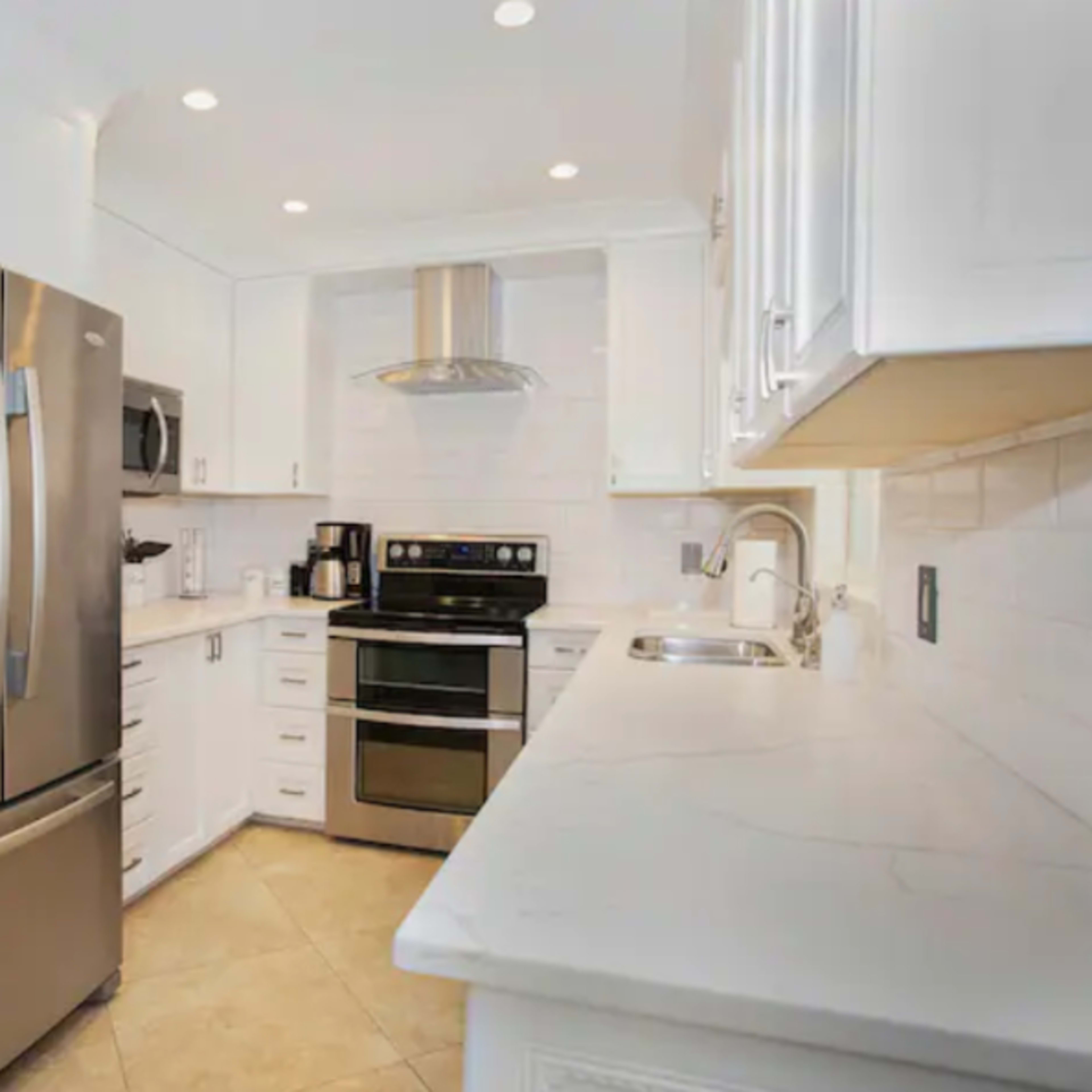 A modern kitchen features stainless steel appliances, white cabinetry, and a marble countertop.