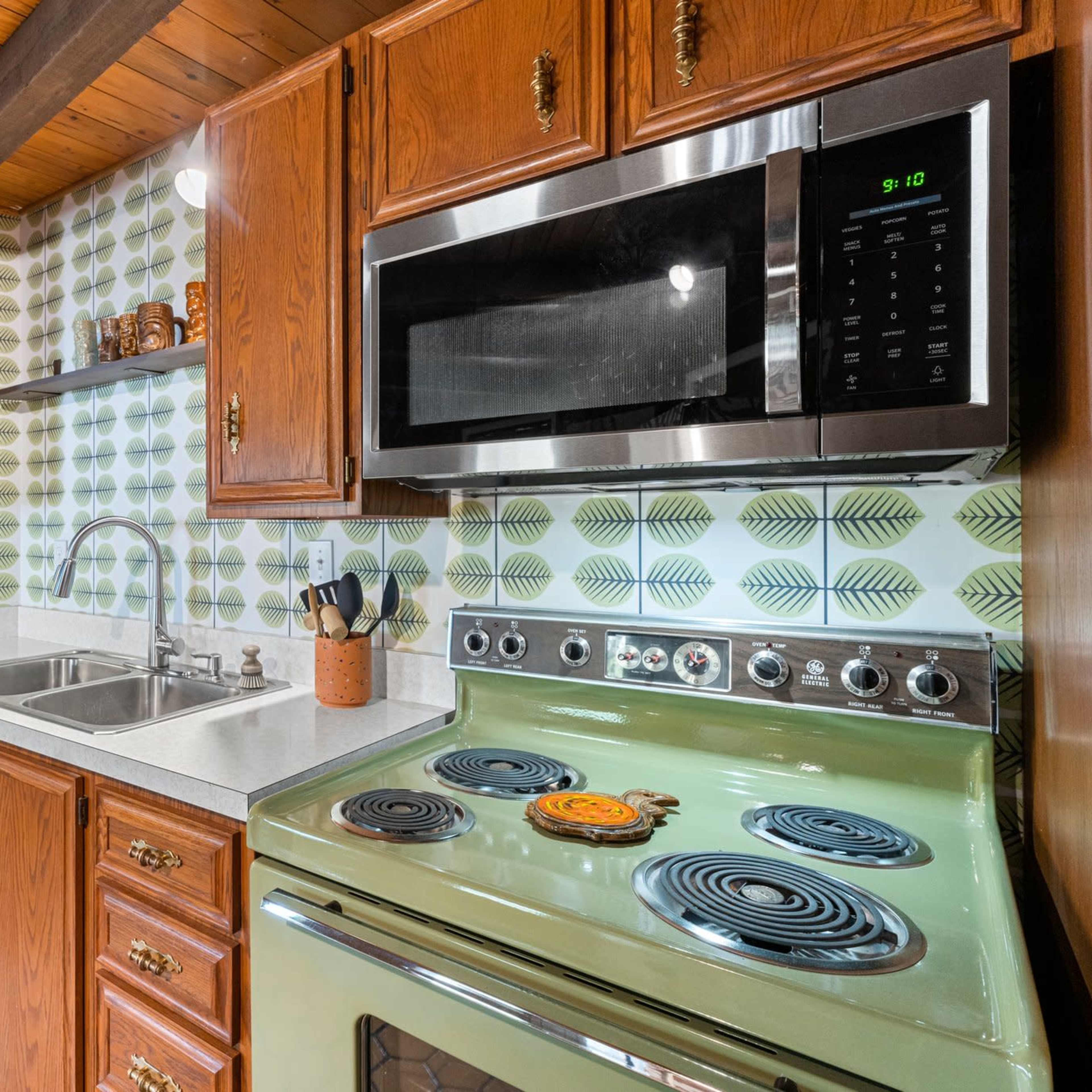 A kitchen featuring wooden cabinetry, a green stove, a stainless steel microwave, and a double sink with a patterned backsplash.