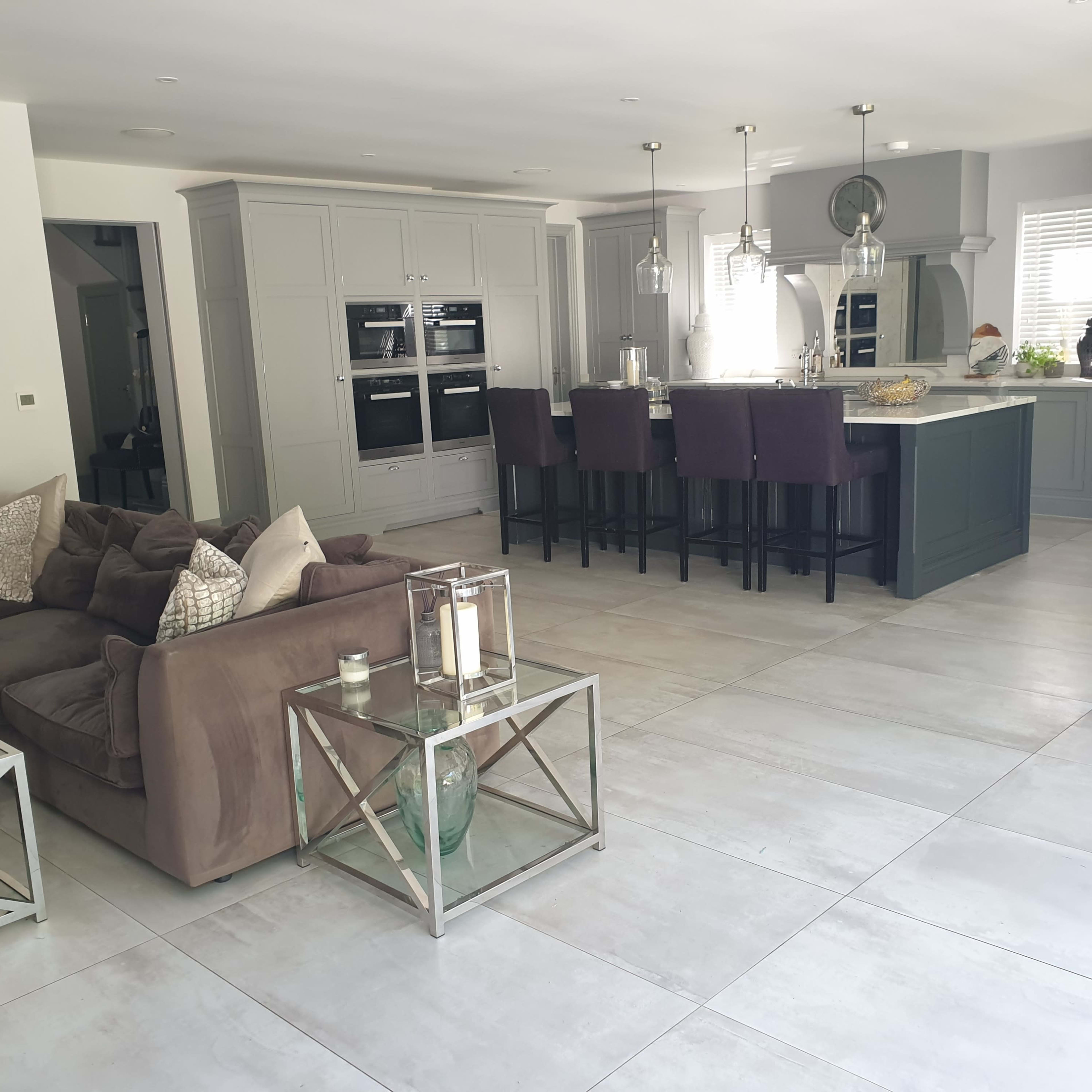A modern, open-concept living space featuring a kitchen with dark cabinetry and bar stools, adjacent to a living area with a large sofa and glass coffee tables.