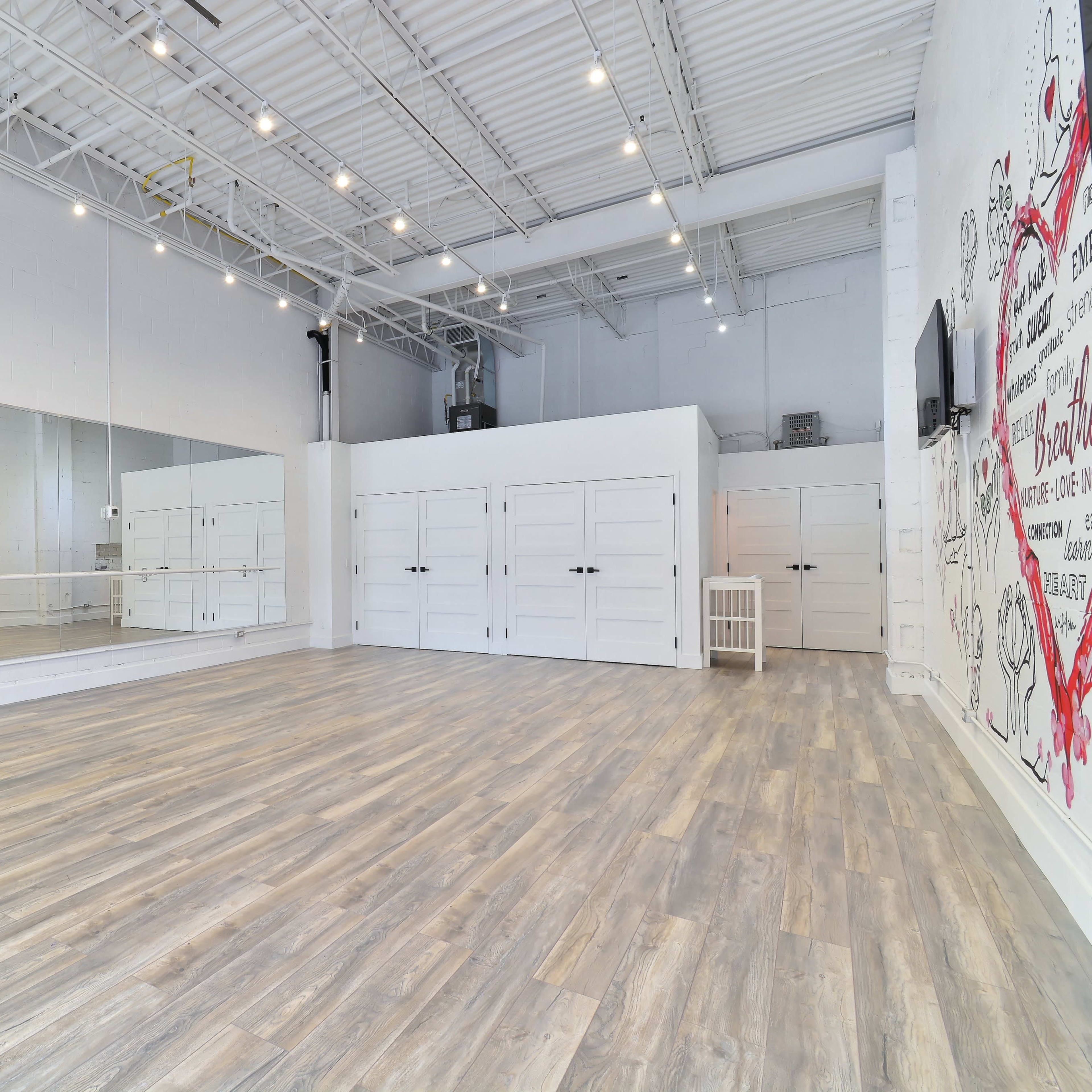 A spacious dance studio with wooden flooring, mirrored walls, and white storage cabinets.