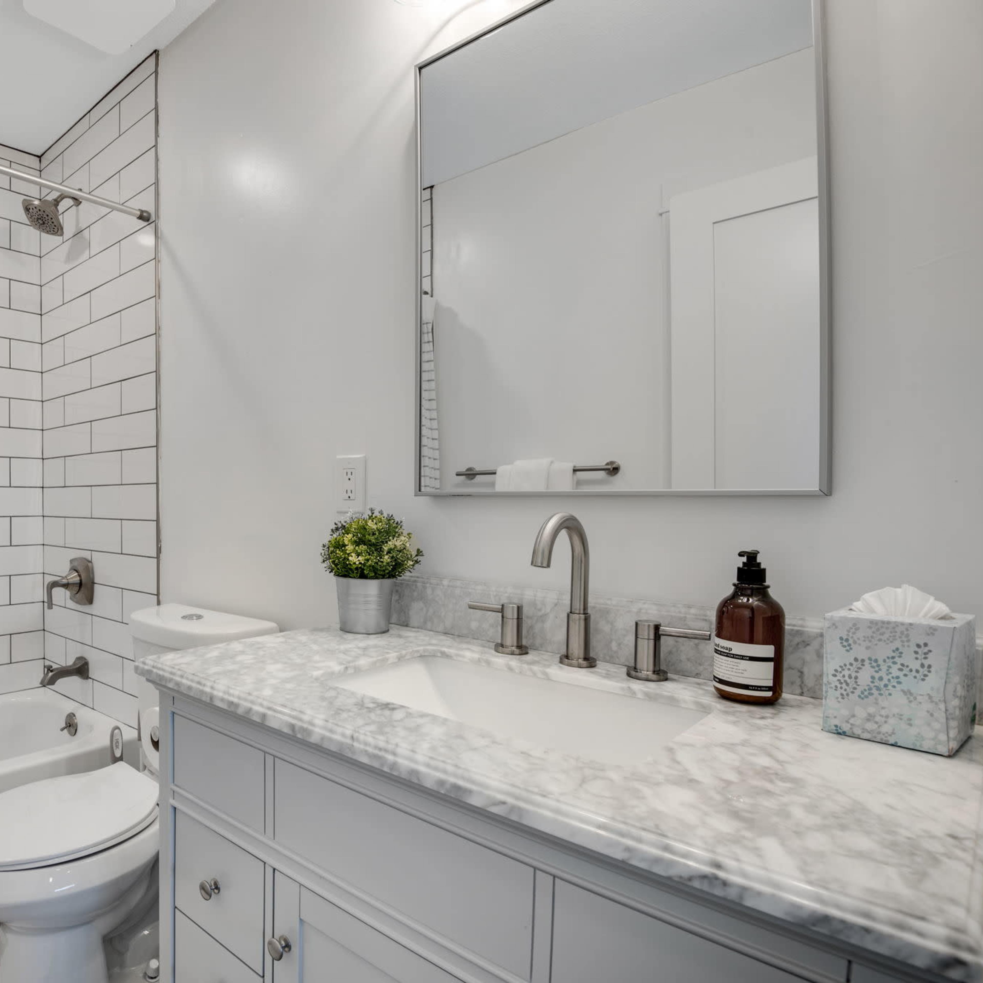 A modern bathroom with a tiled shower, a white bathtub, a marble countertop sink, and a wooden vanity.