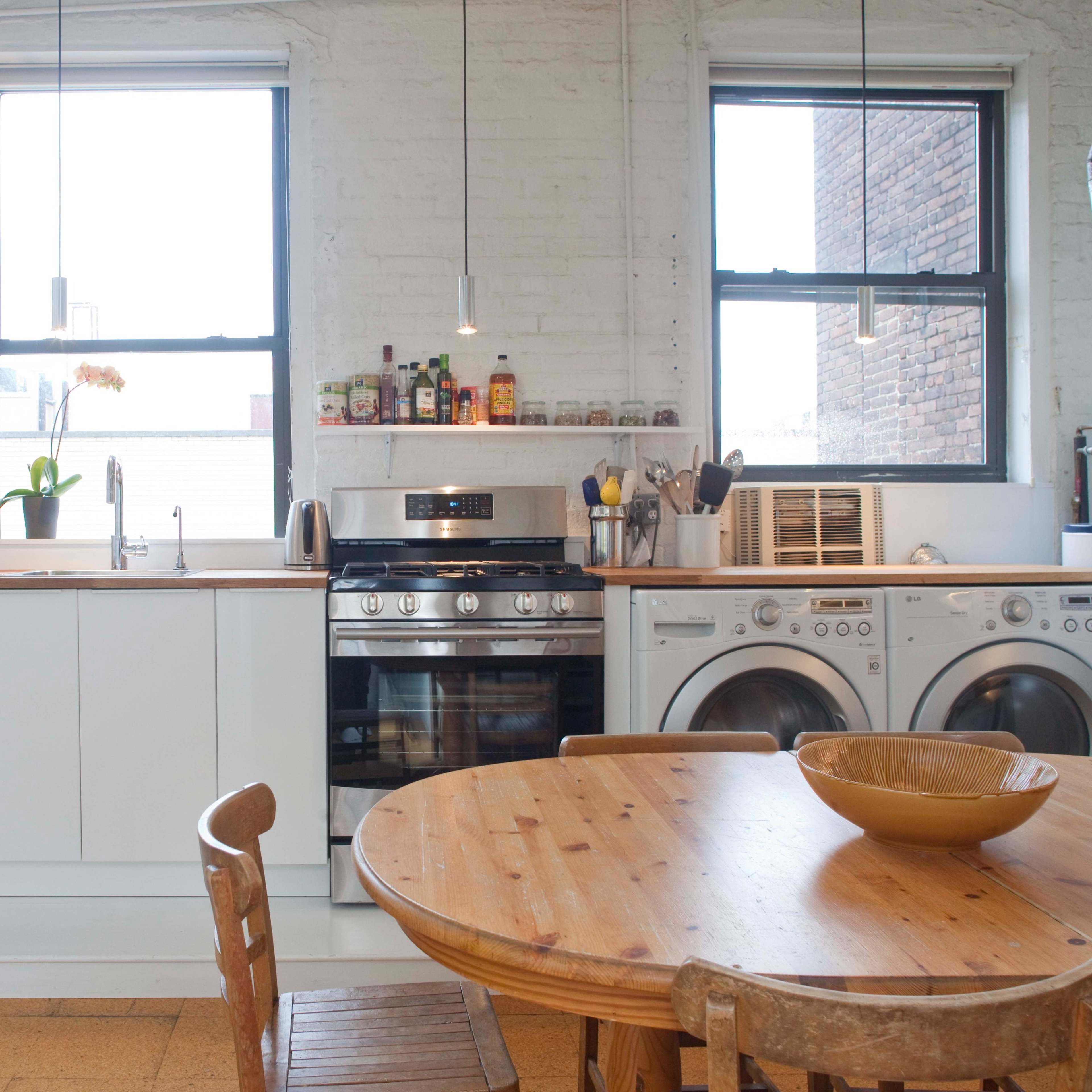 A bright kitchen features a wooden table, modern appliances, and a large window allowing natural light to fill the space.
