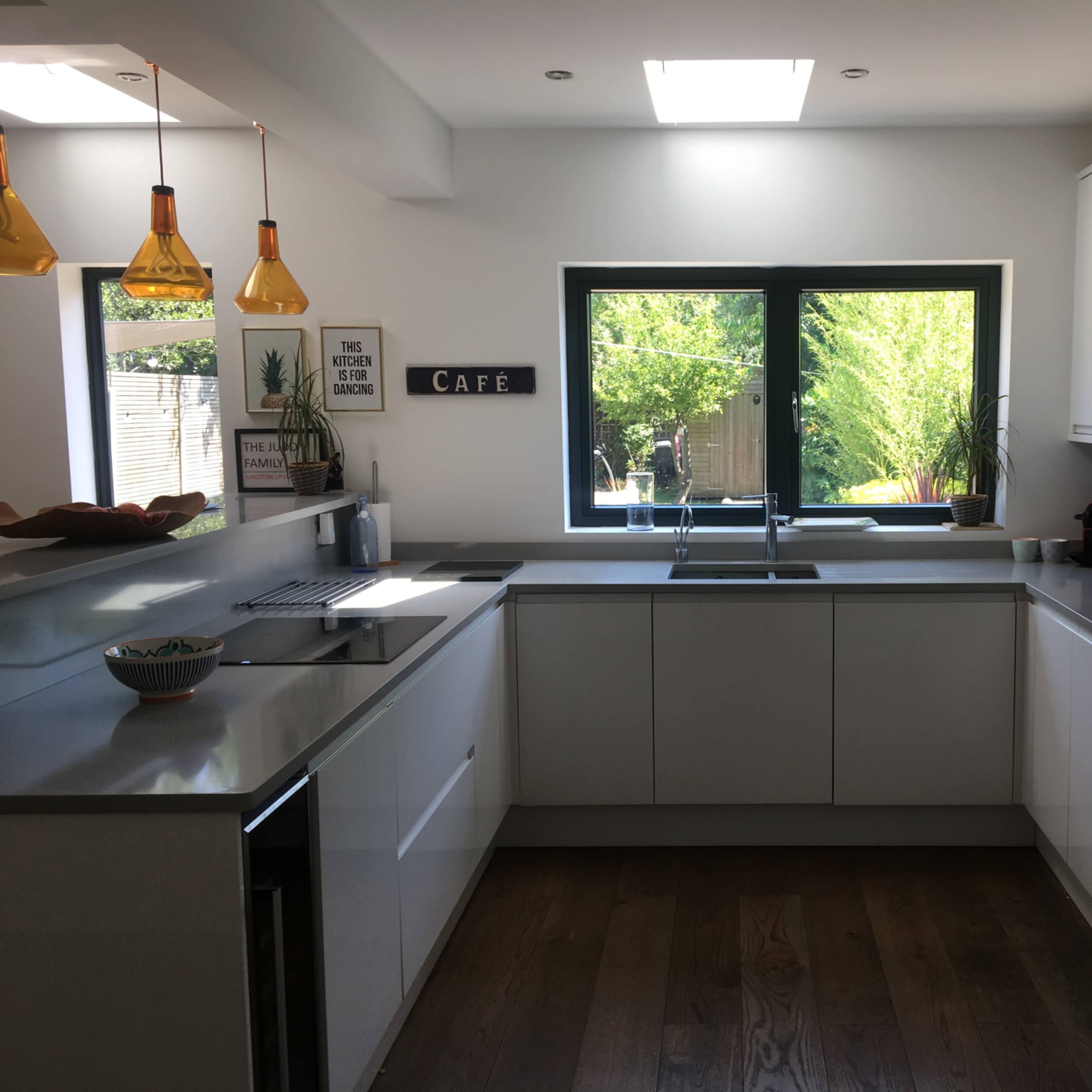 A modern kitchen with white cabinets, a central island, and large windows that provide natural light and a view of greenery outside.
