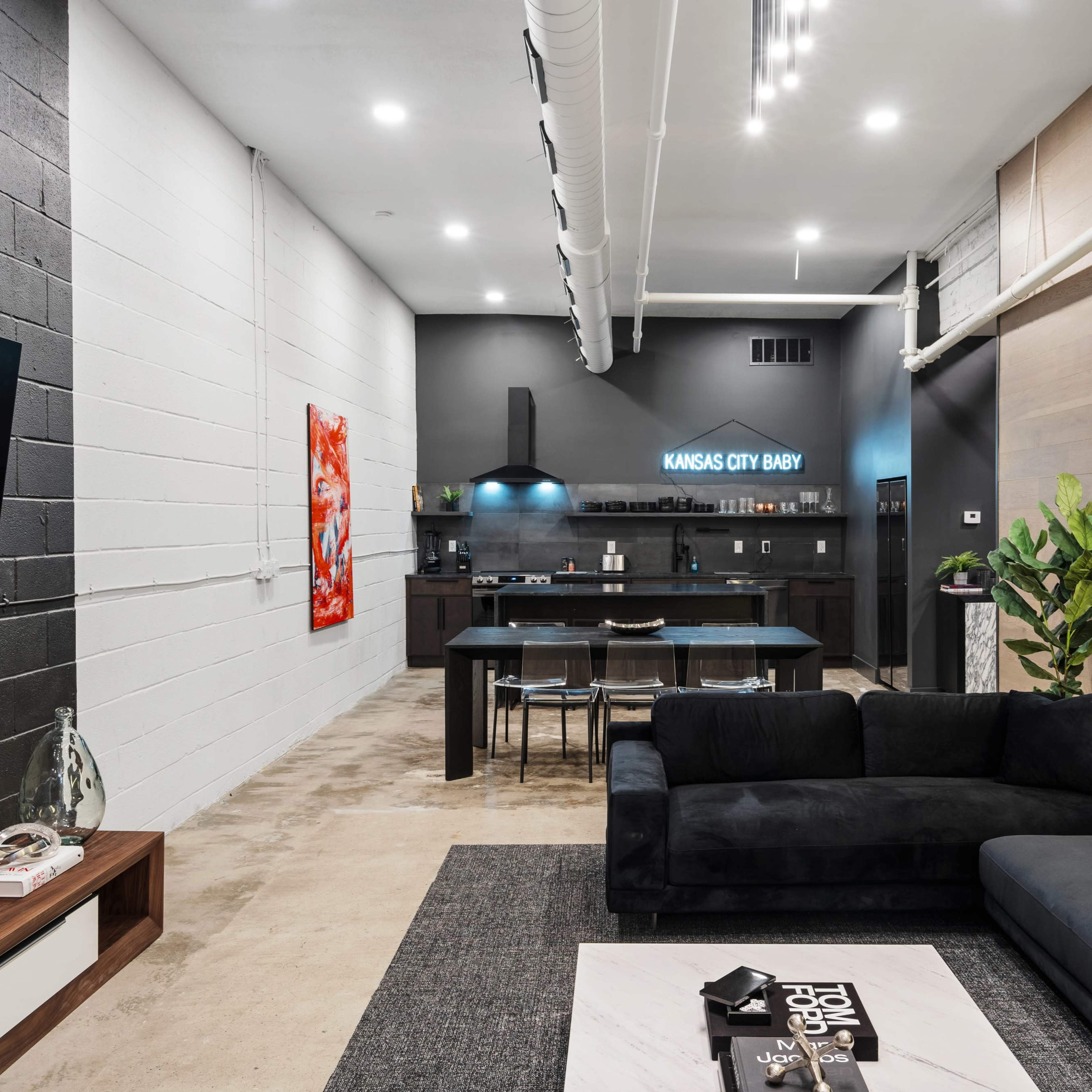 A modern, stylish living space featuring a black sectional sofa, a coffee table, and an open kitchen at the far end with sleek cabinetry.