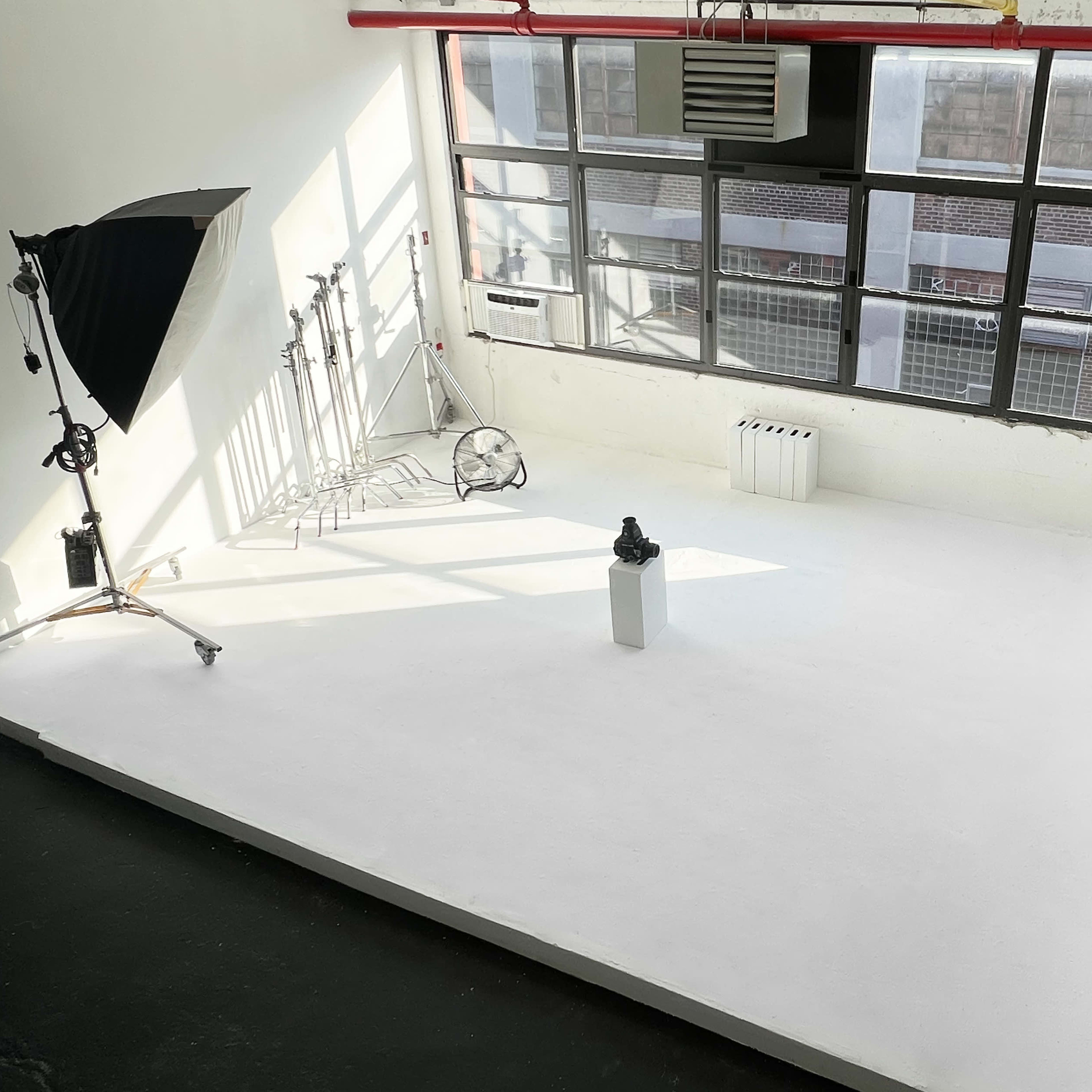 A well-lit photography studio with a white backdrop, a lighting setup, and a variety of colorful rolls of backdrops arranged on the side.