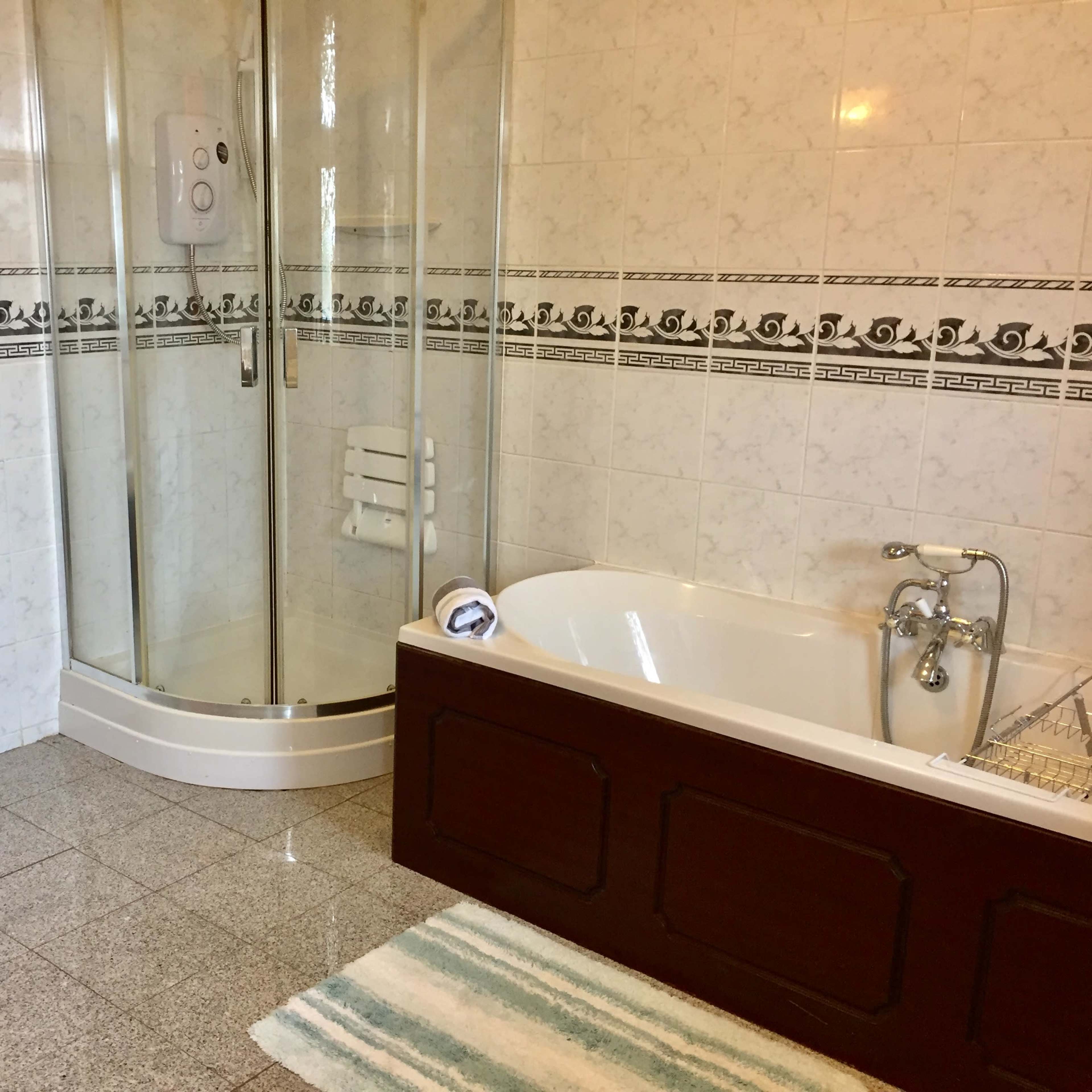 A bathroom featuring a glass shower enclosure, a white bathtub with a wooden panel, and tiled walls.