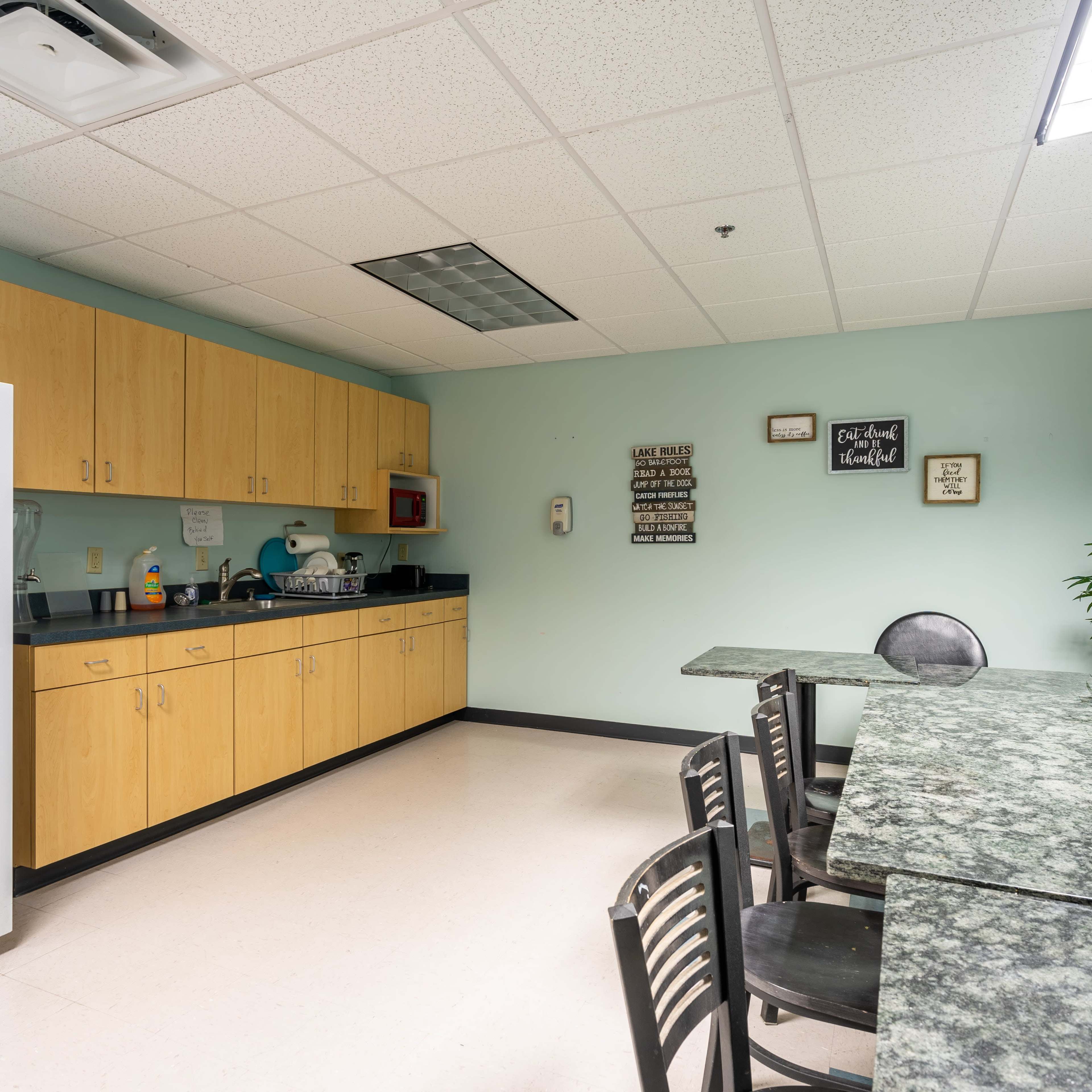 A kitchen area with wooden cabinets, a white refrigerator, a microwave, and a granite-topped table with chairs.