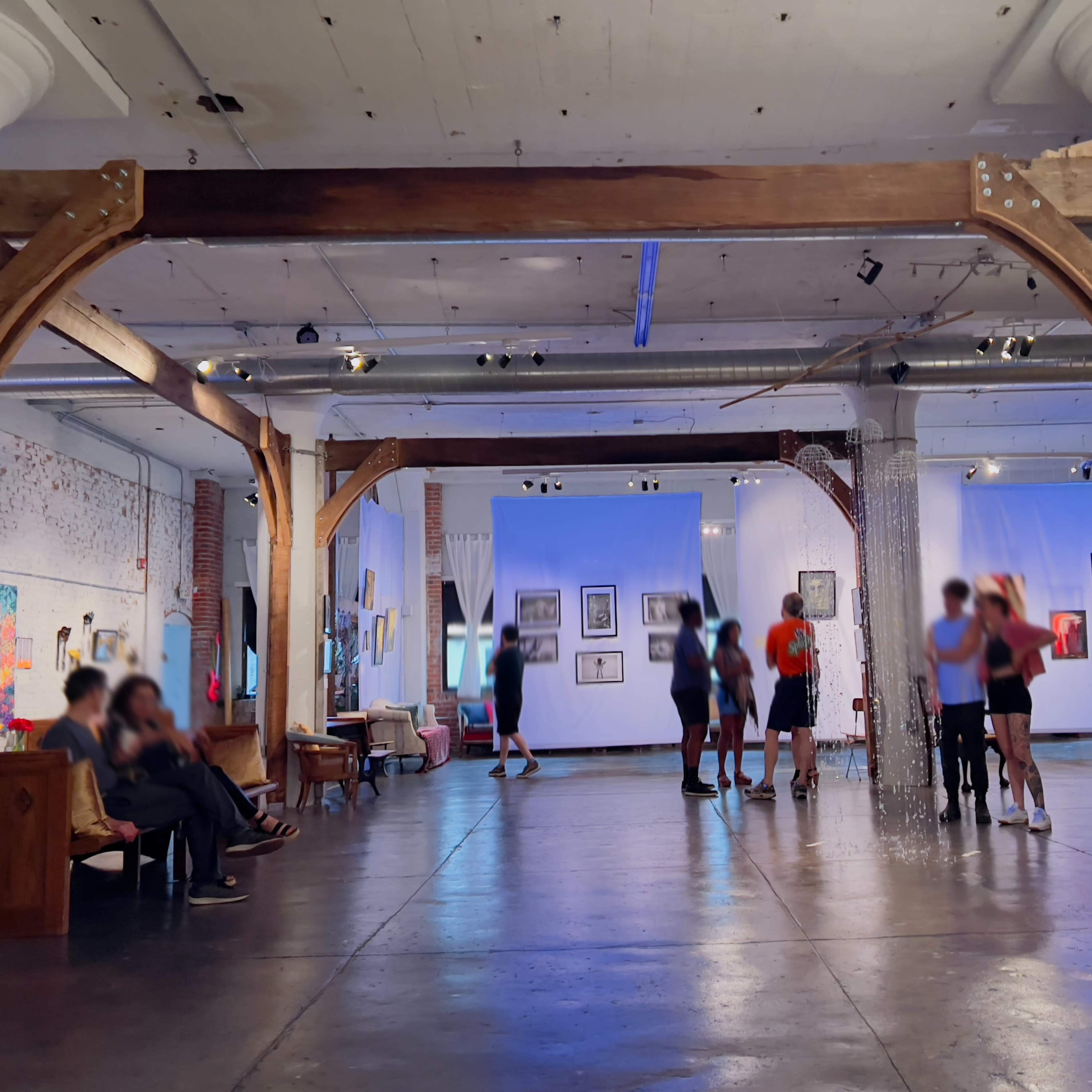 An art gallery with wooden beams, people engaging in activities, and various artworks displayed on the walls.
