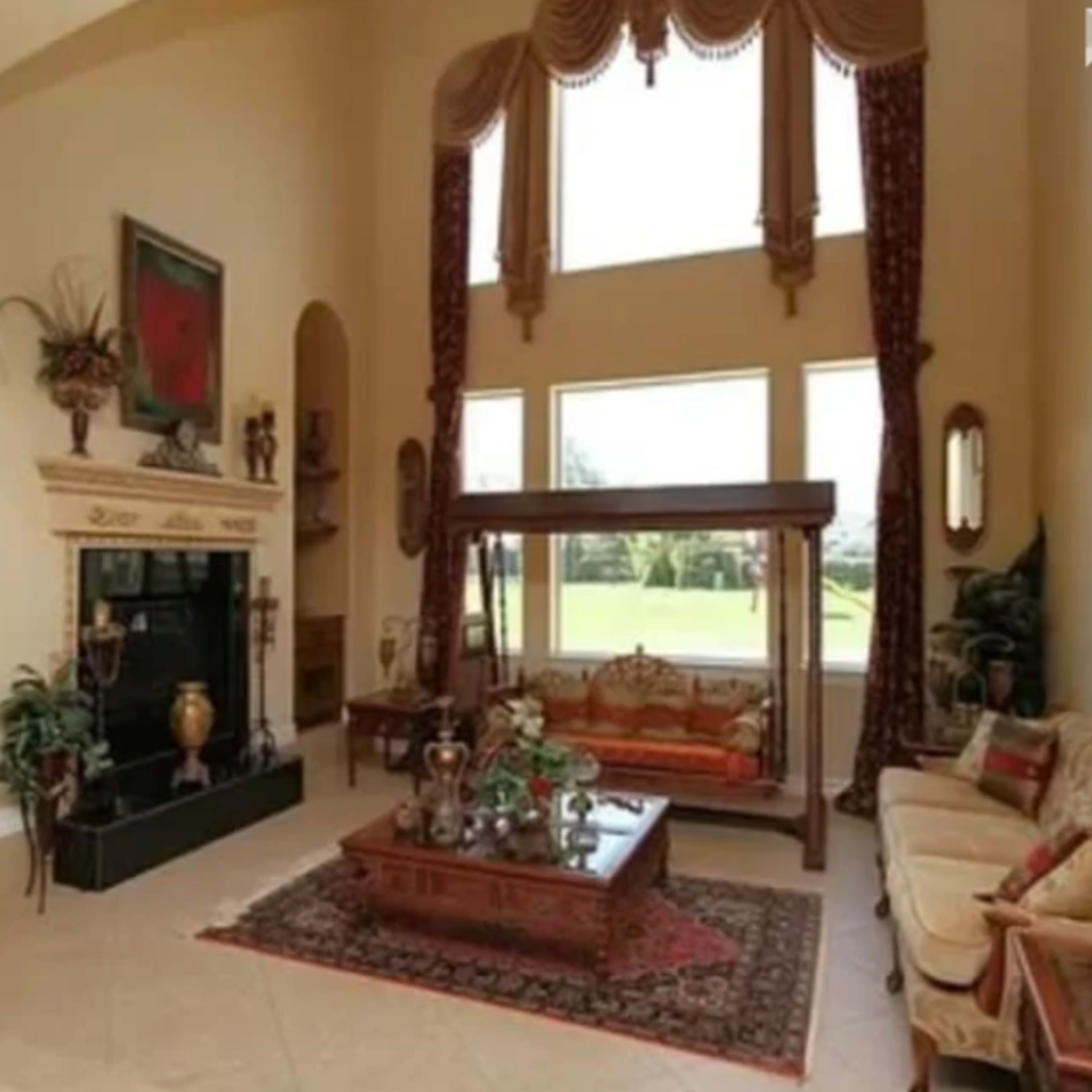 A spacious living room featuring high ceilings, large windows, and elegant furniture arranged around a central area rug.