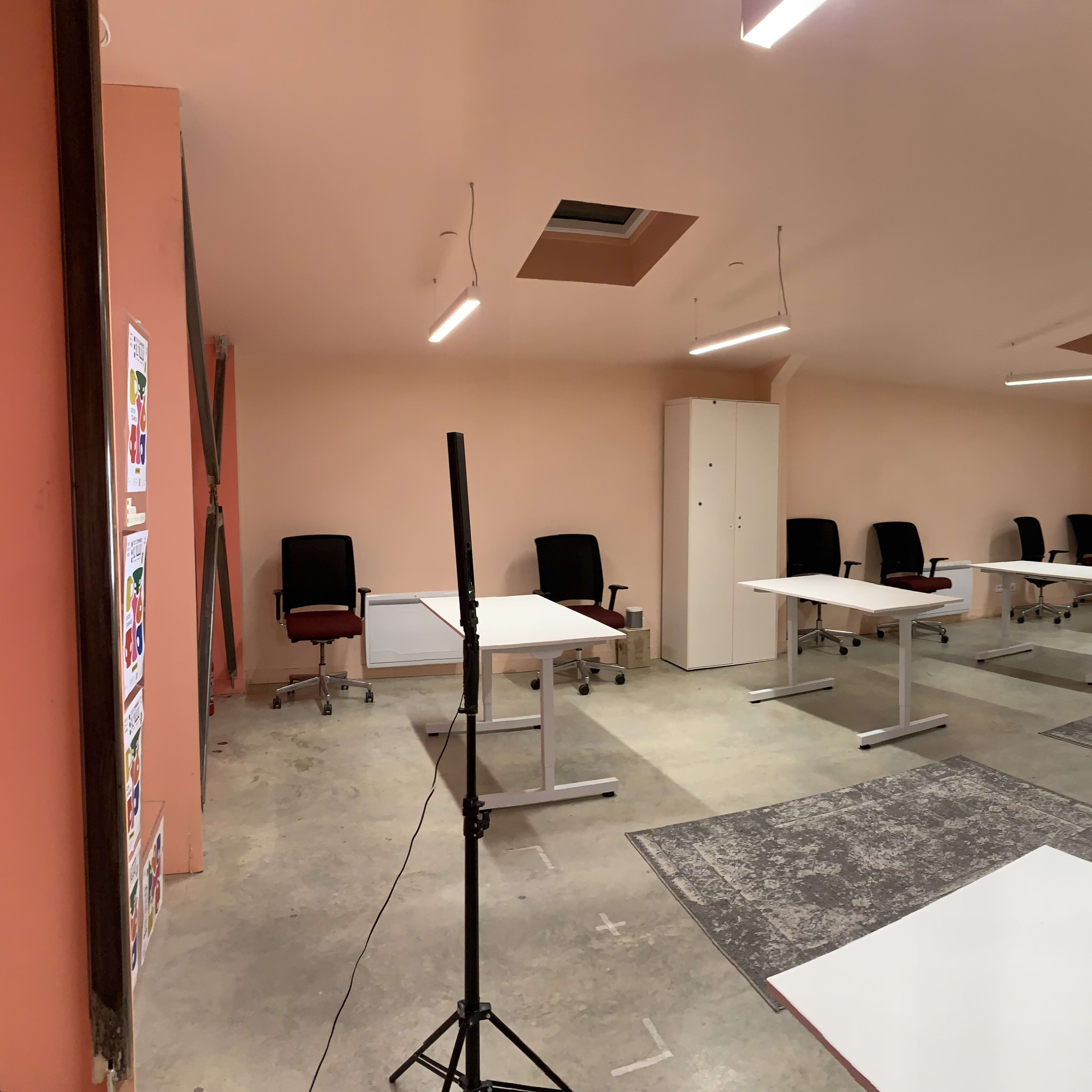 A spacious, empty office with several desks arranged in rows and chairs placed at them, all under bright overhead lighting.