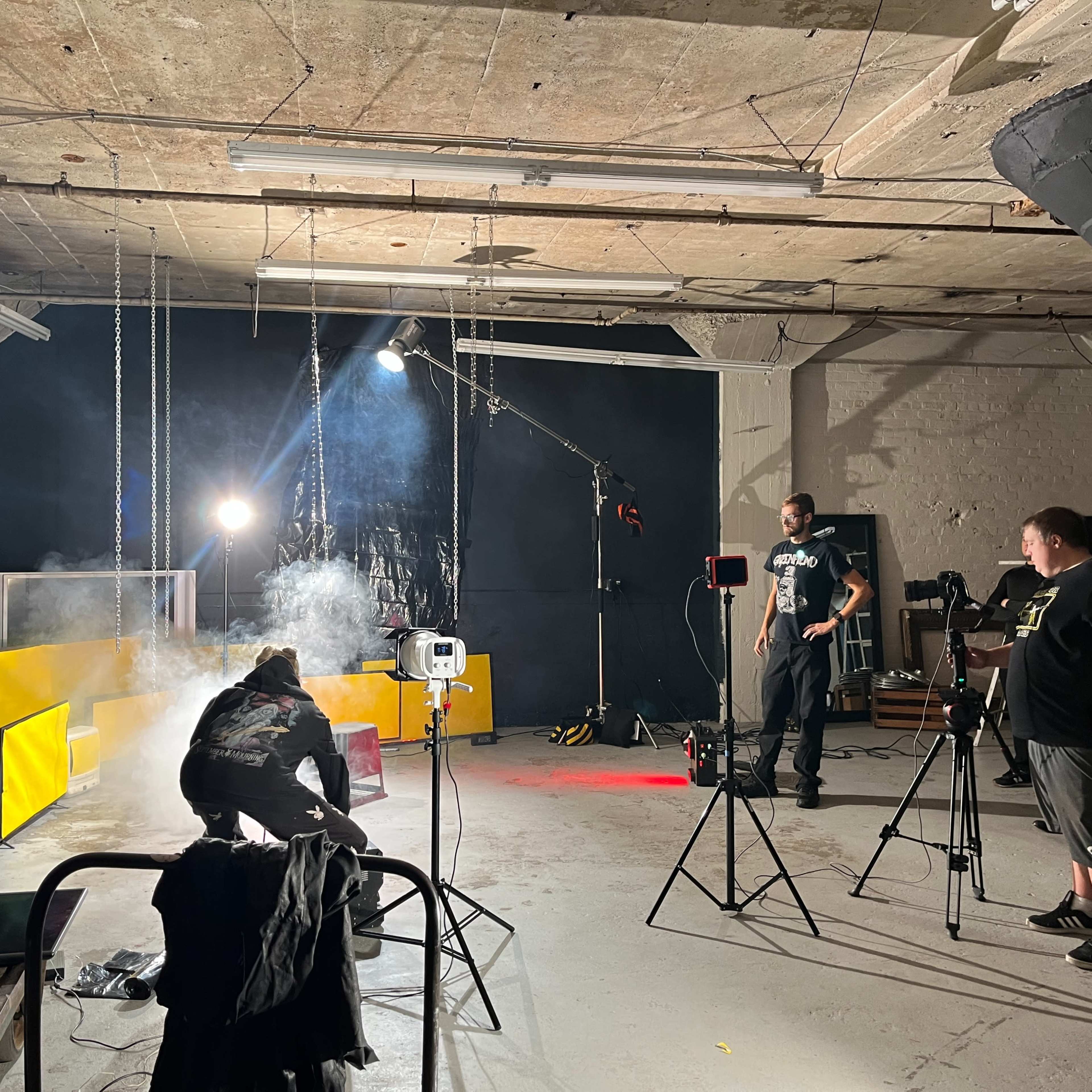 A group of people is setting up a photo shoot in an industrial room with yellow furniture and various lighting equipment.
