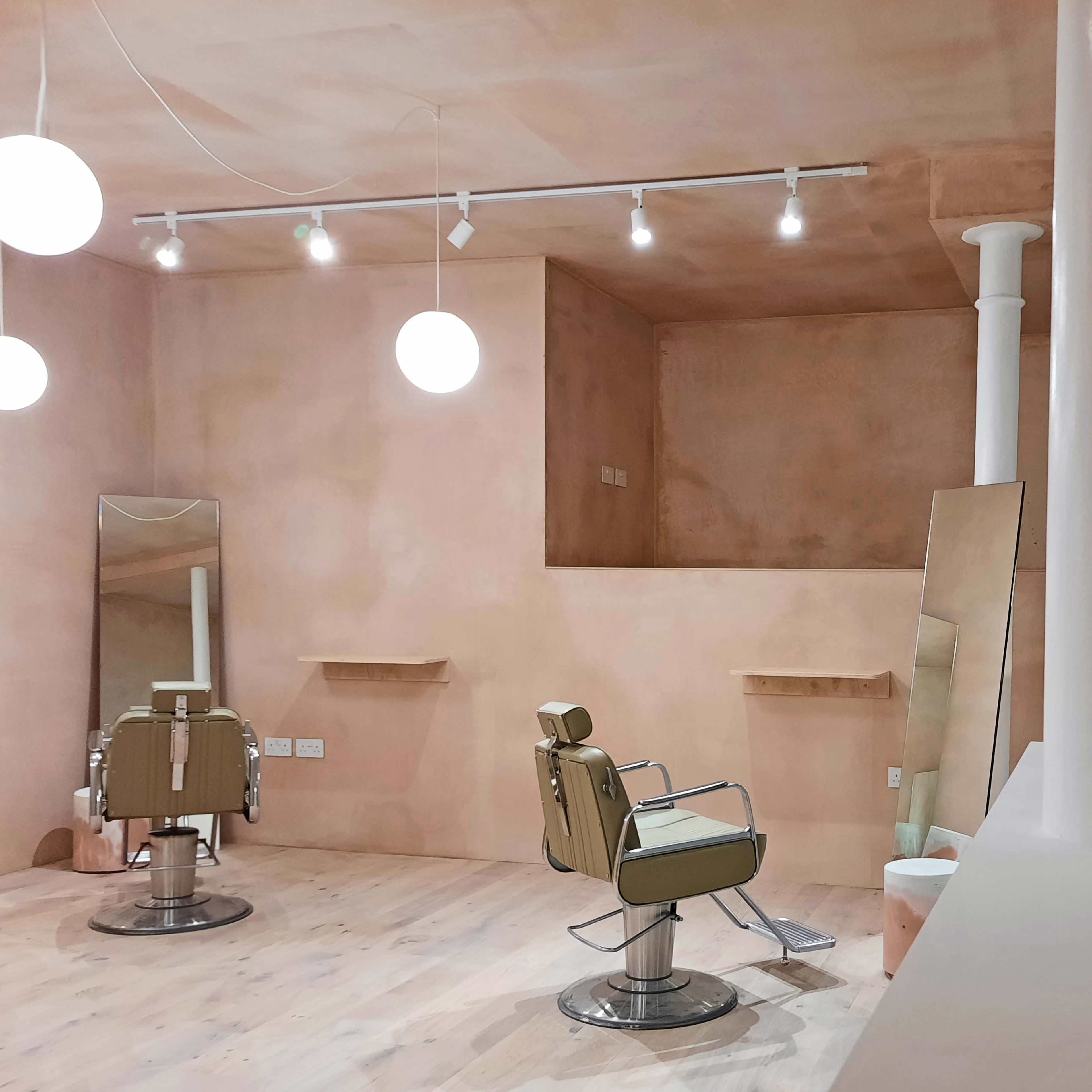 A minimalist hair salon with two styling chairs and large mirrors against a softly colored, smooth wall.