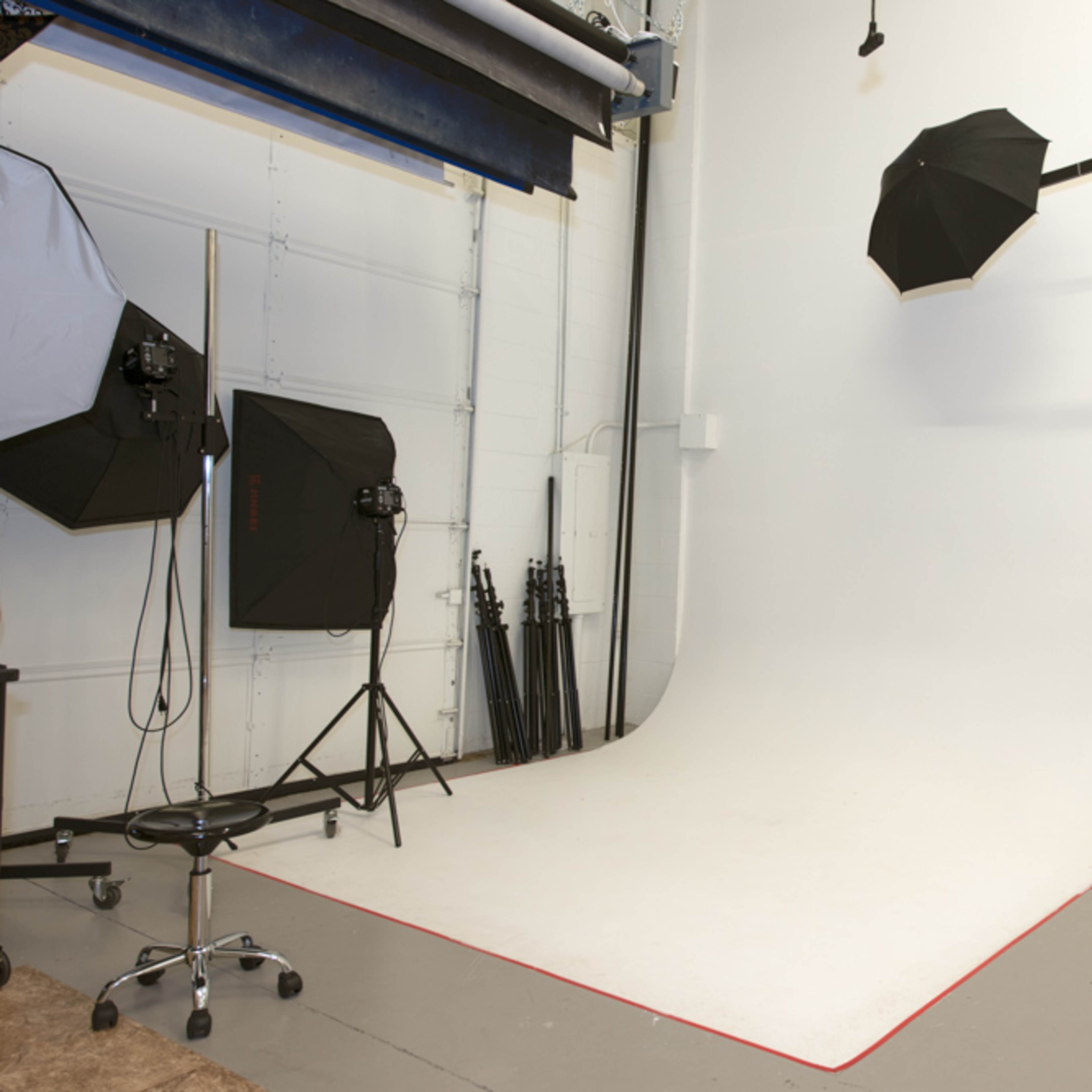 A photography studio features a white curved backdrop with lighting equipment and tripods arranged around it.