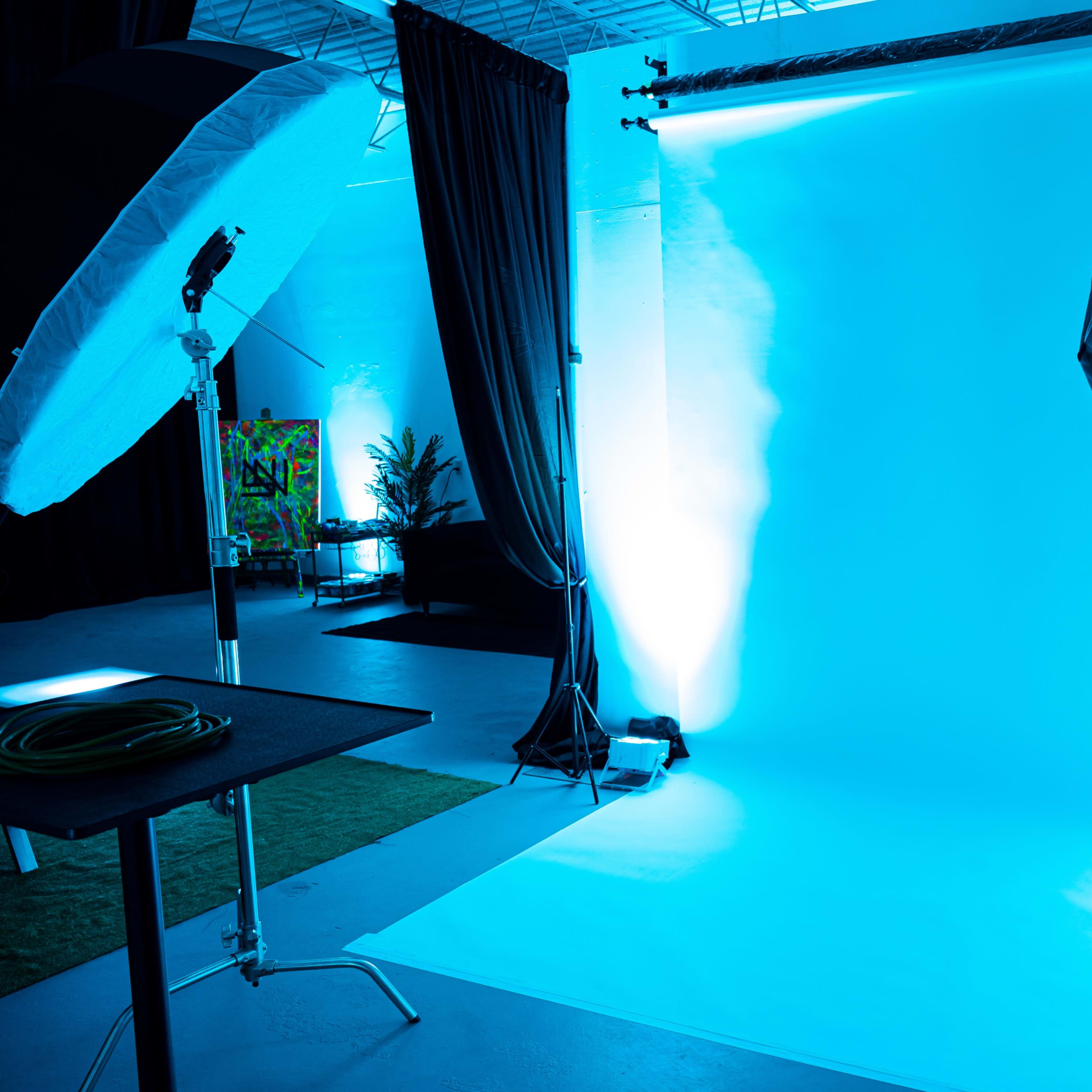 A photography studio setup with an illuminated blue backdrop and two large softbox lights on either side.