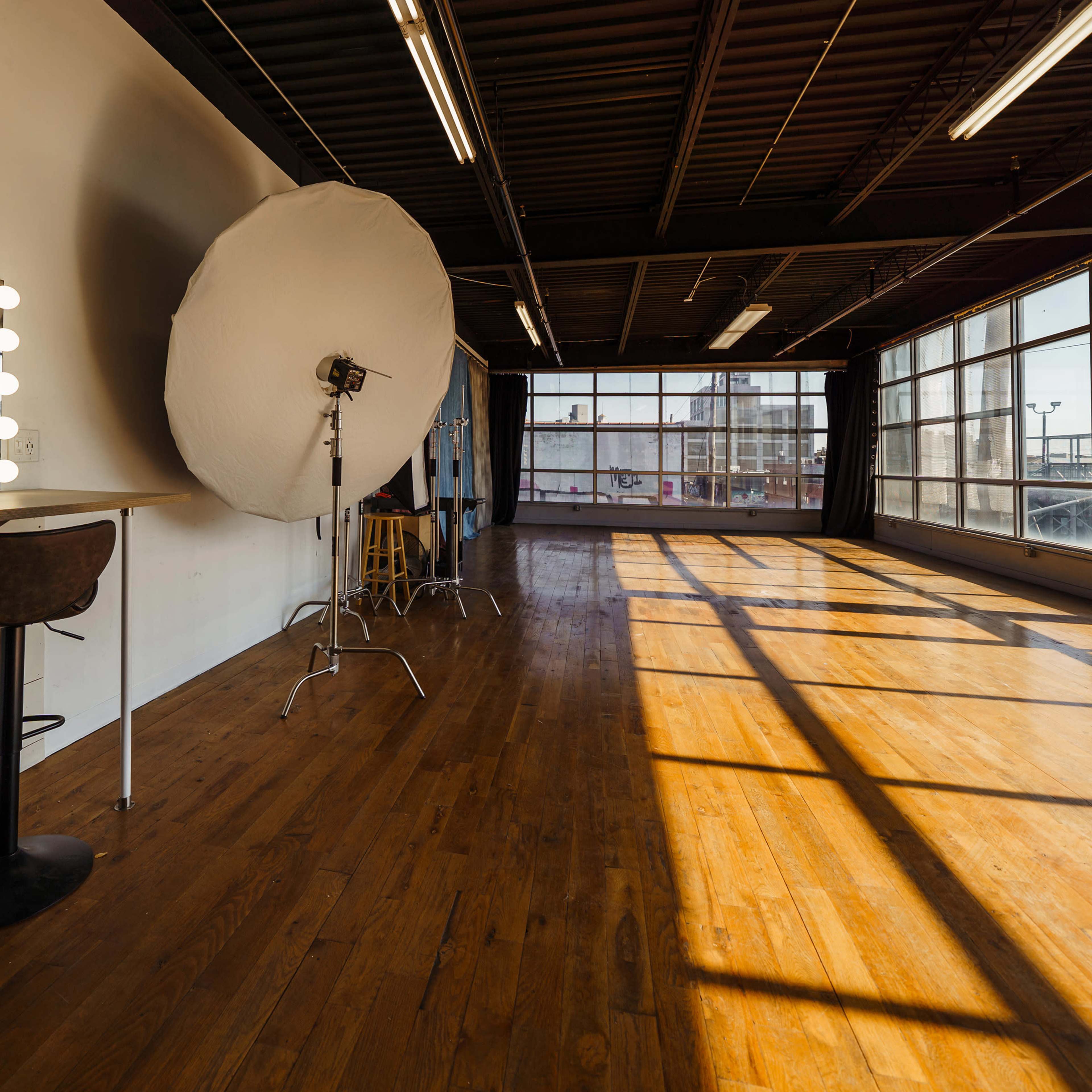 A photography studio with a mirror surrounded by lights, a softbox, and wooden flooring.