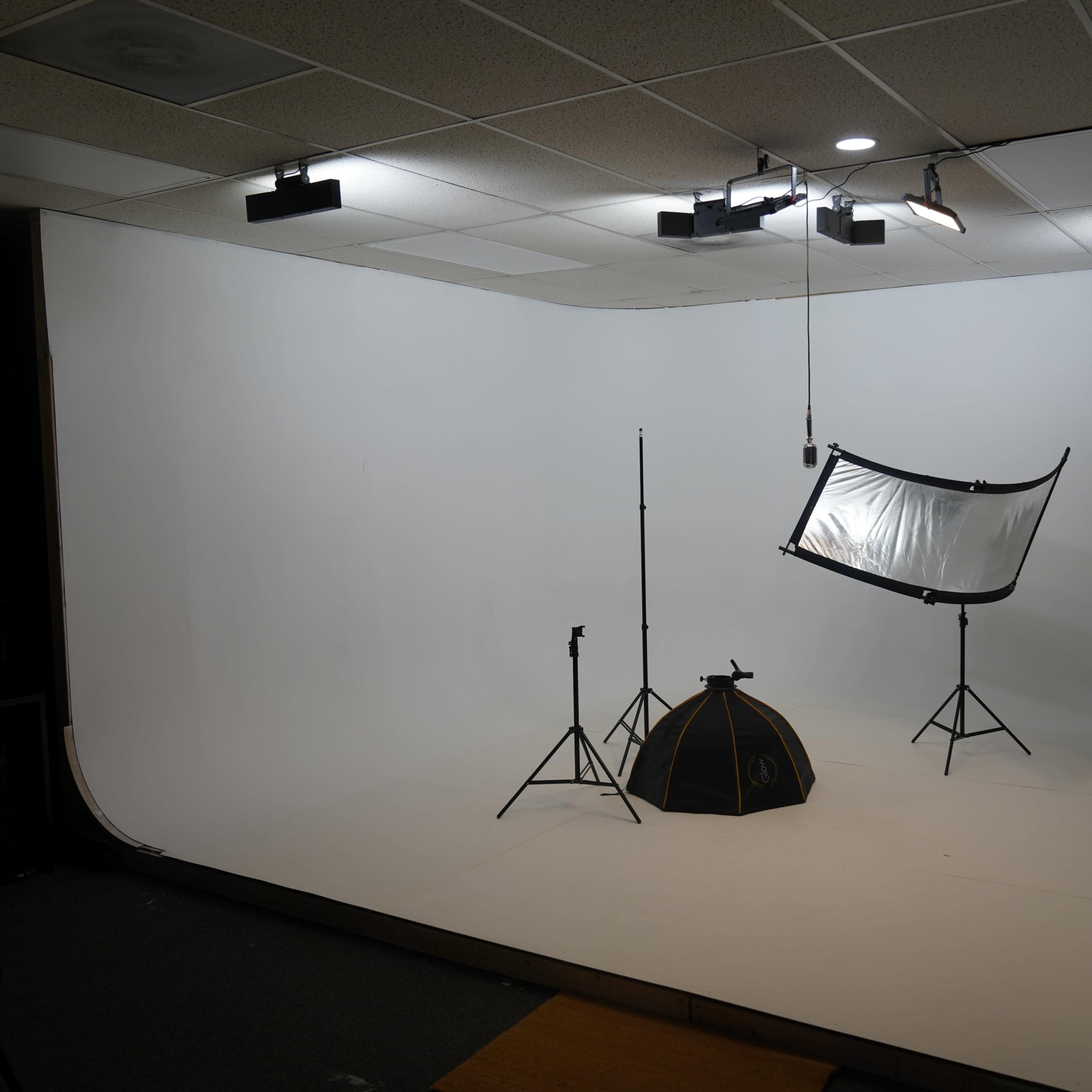A photography studio featuring a seamless white backdrop, light stands, and a large reflector set up on a raised platform.