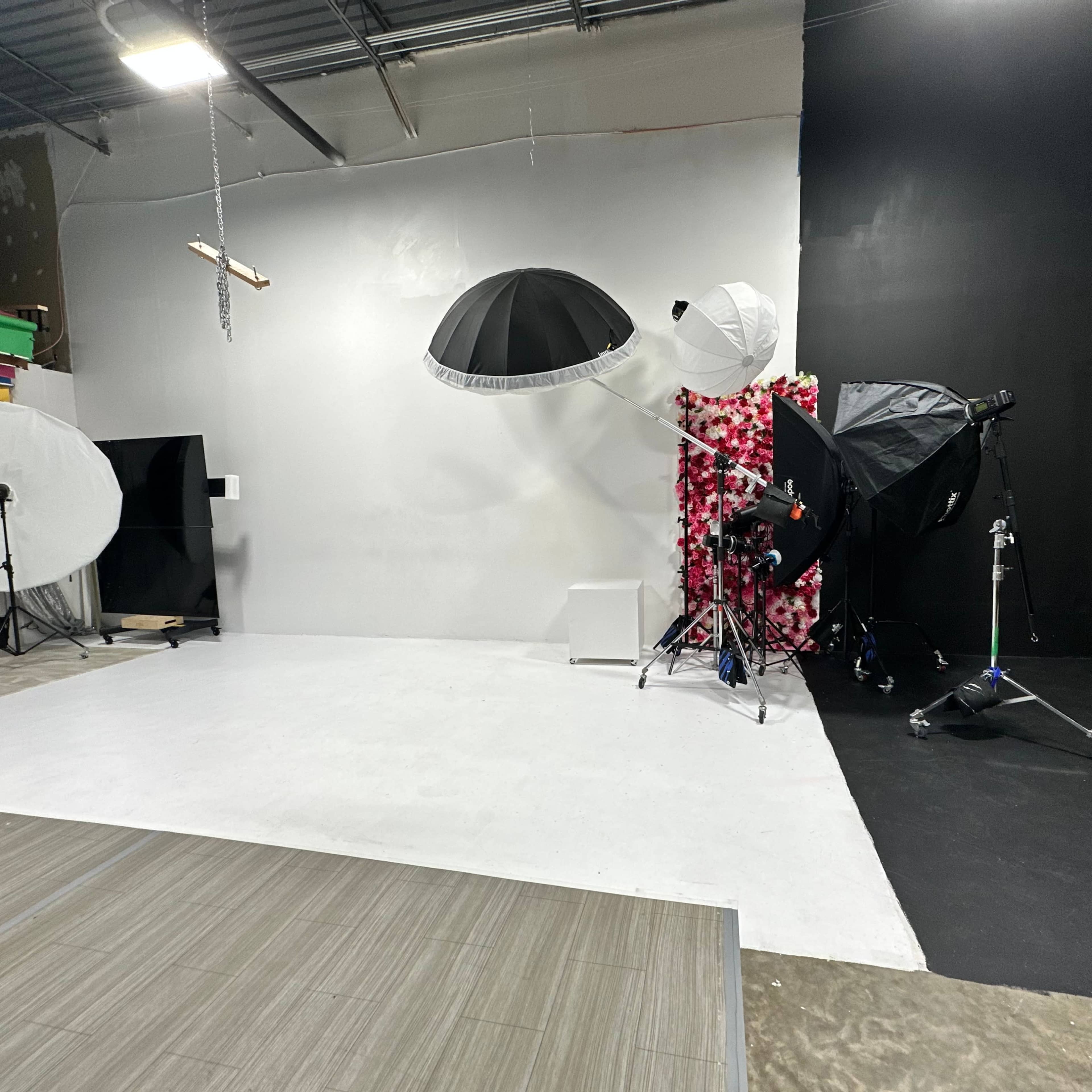 A professional photography studio with various lighting equipment, backdrops, and a large white floor space.