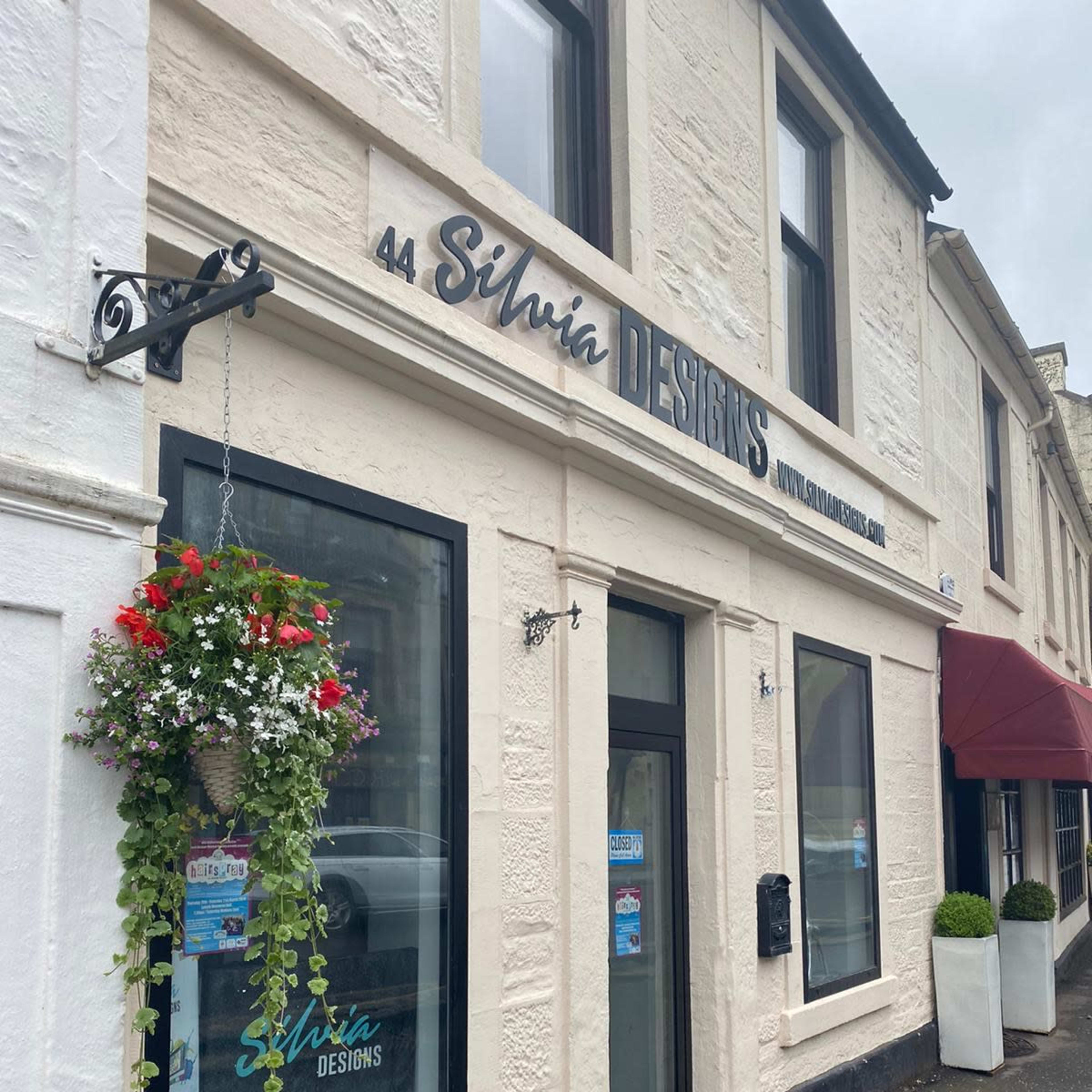 The storefront of Silvia Designs, located at 44, features a sign above the entrance and hanging flower baskets.