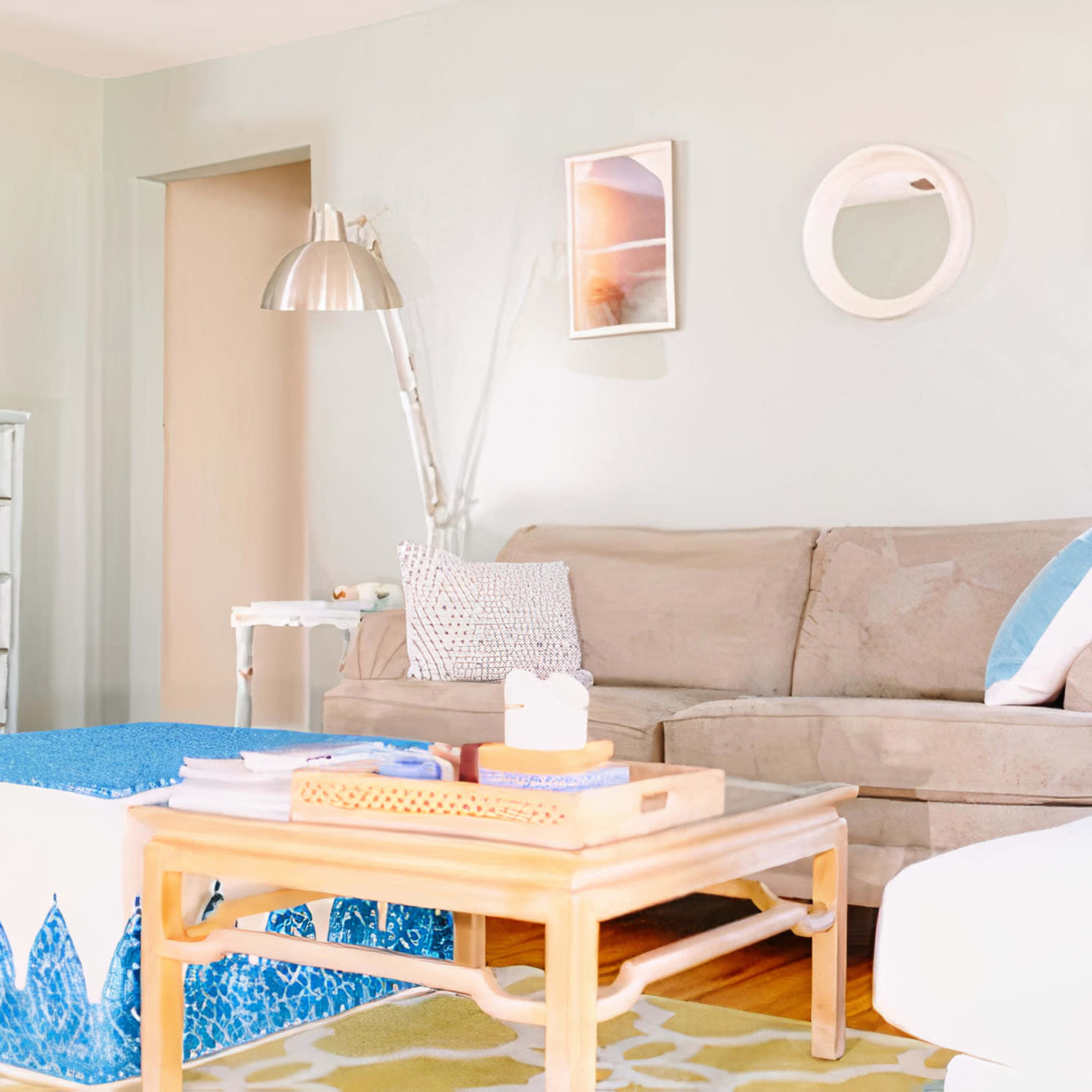 A light and airy living room features a beige sofa, a blue-patterned coffee table, and a decorative side cabinet against a pastel wall.