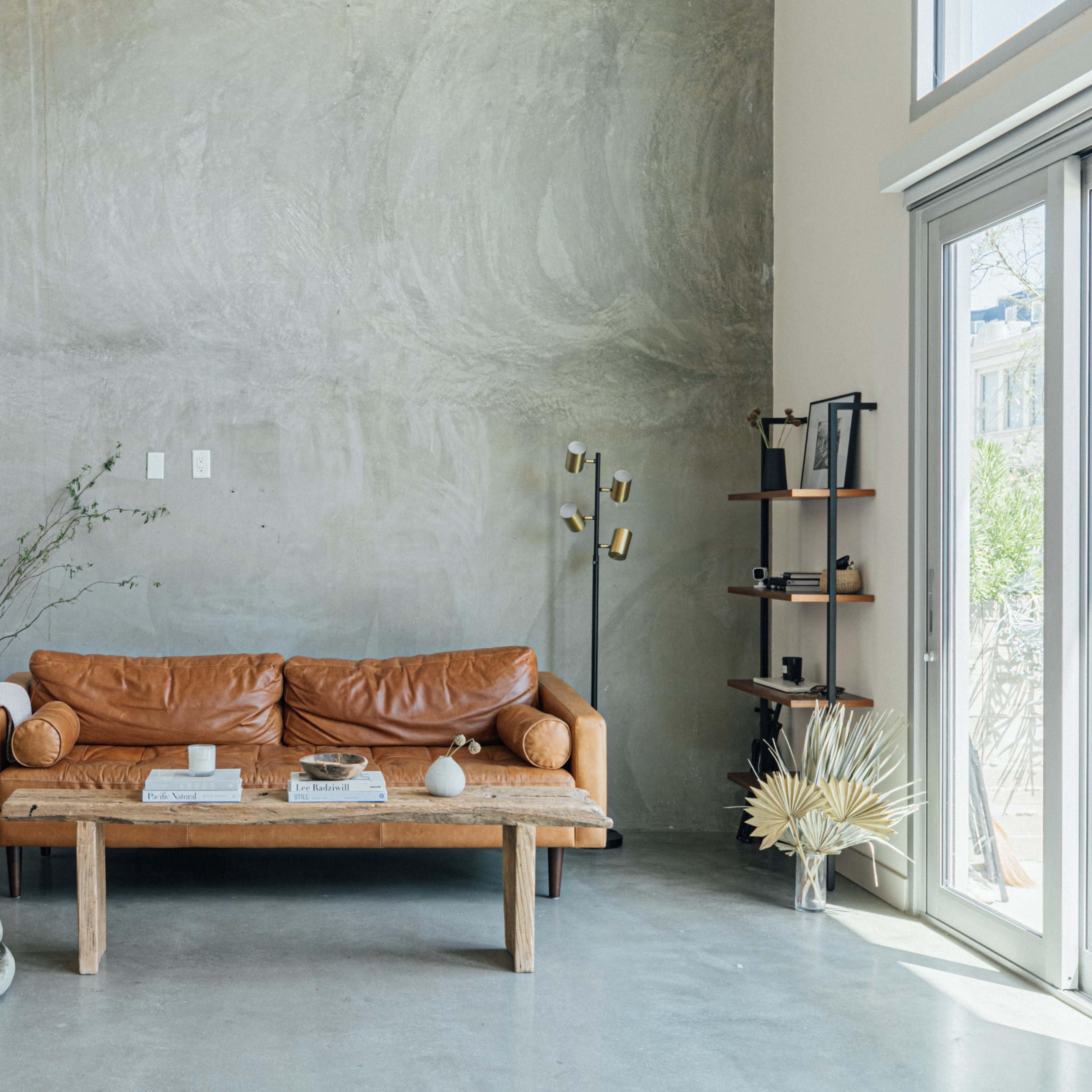 A leather sofa sits against a textured gray wall in a minimalist living room, accompanied by a wooden coffee table and various decorative elements.