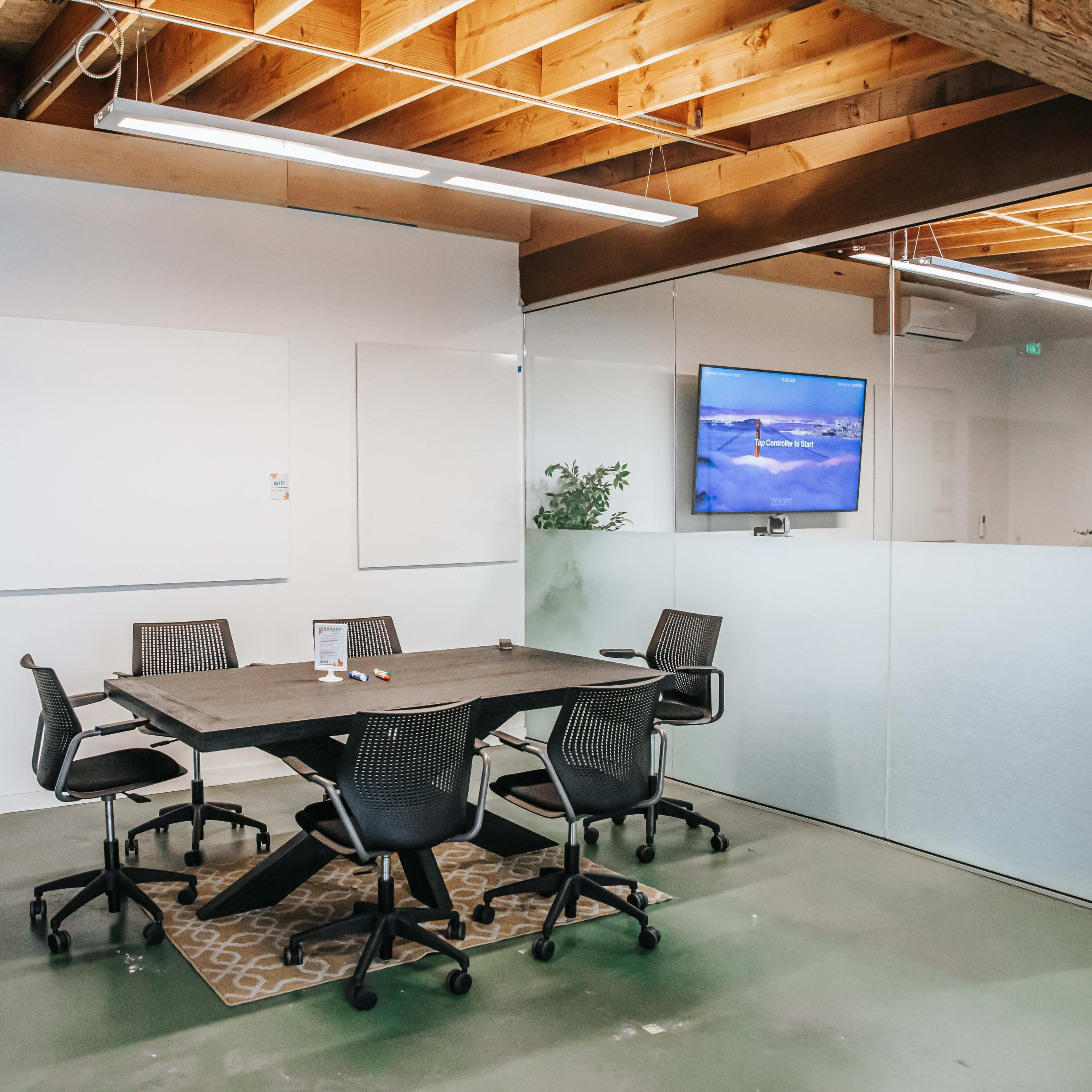 A modern conference room with a large table and several office chairs, featuring a wall-mounted TV and whiteboards.