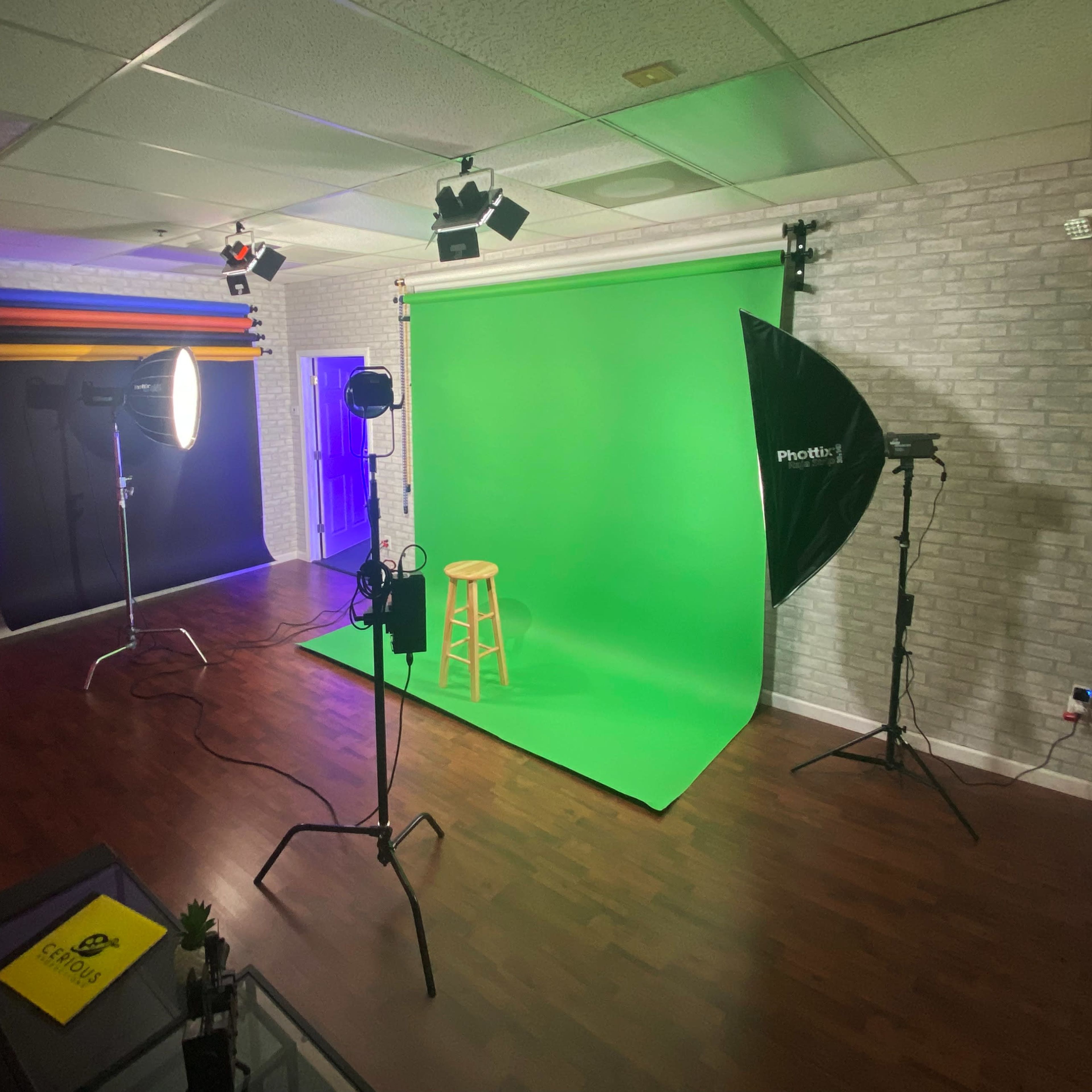 A photography studio equipped with a green backdrop, lighting equipment, and a stool positioned for shooting.
