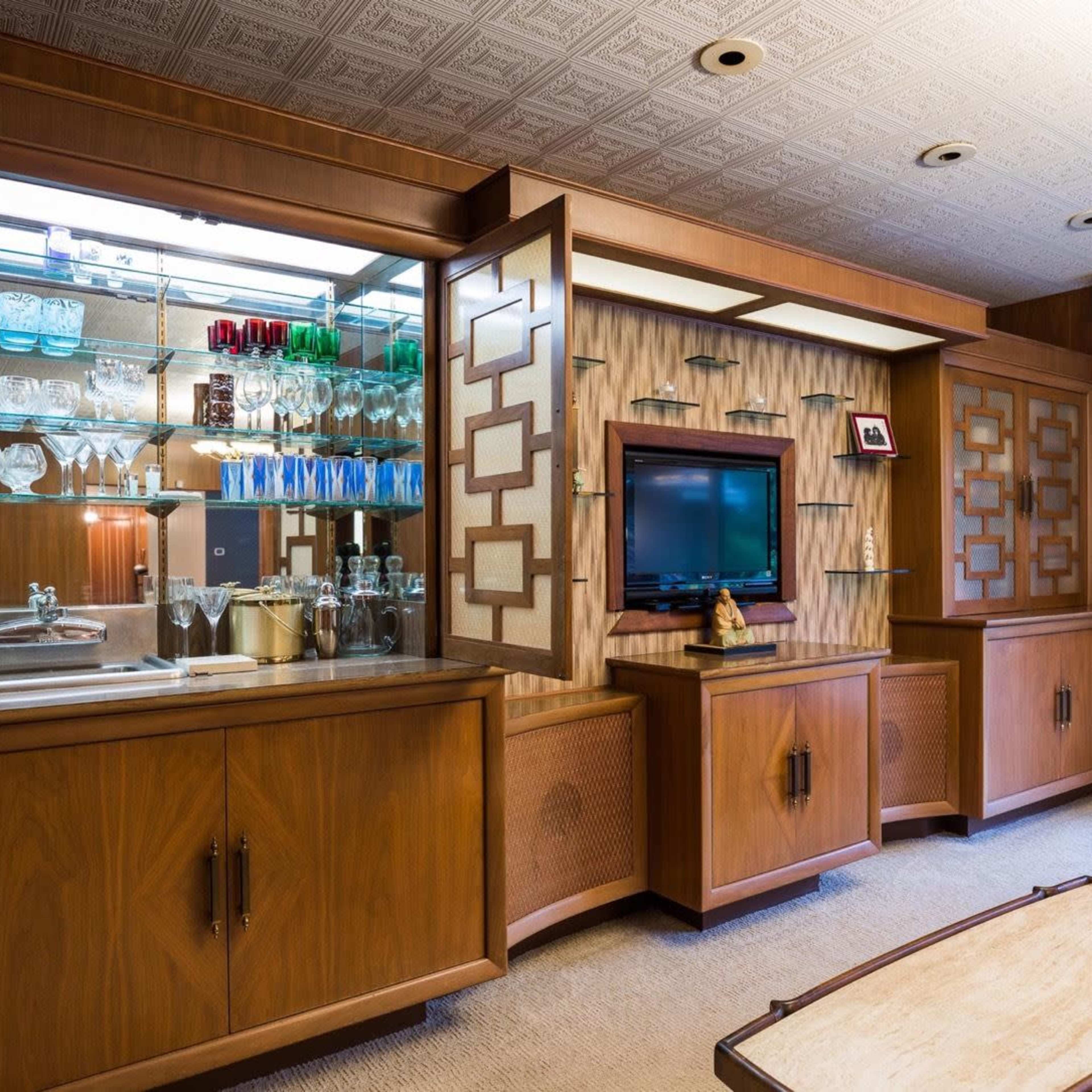 A mid-century modern living room with wooden cabinetry, a glass display cabinet, and a television mounted on the wall.