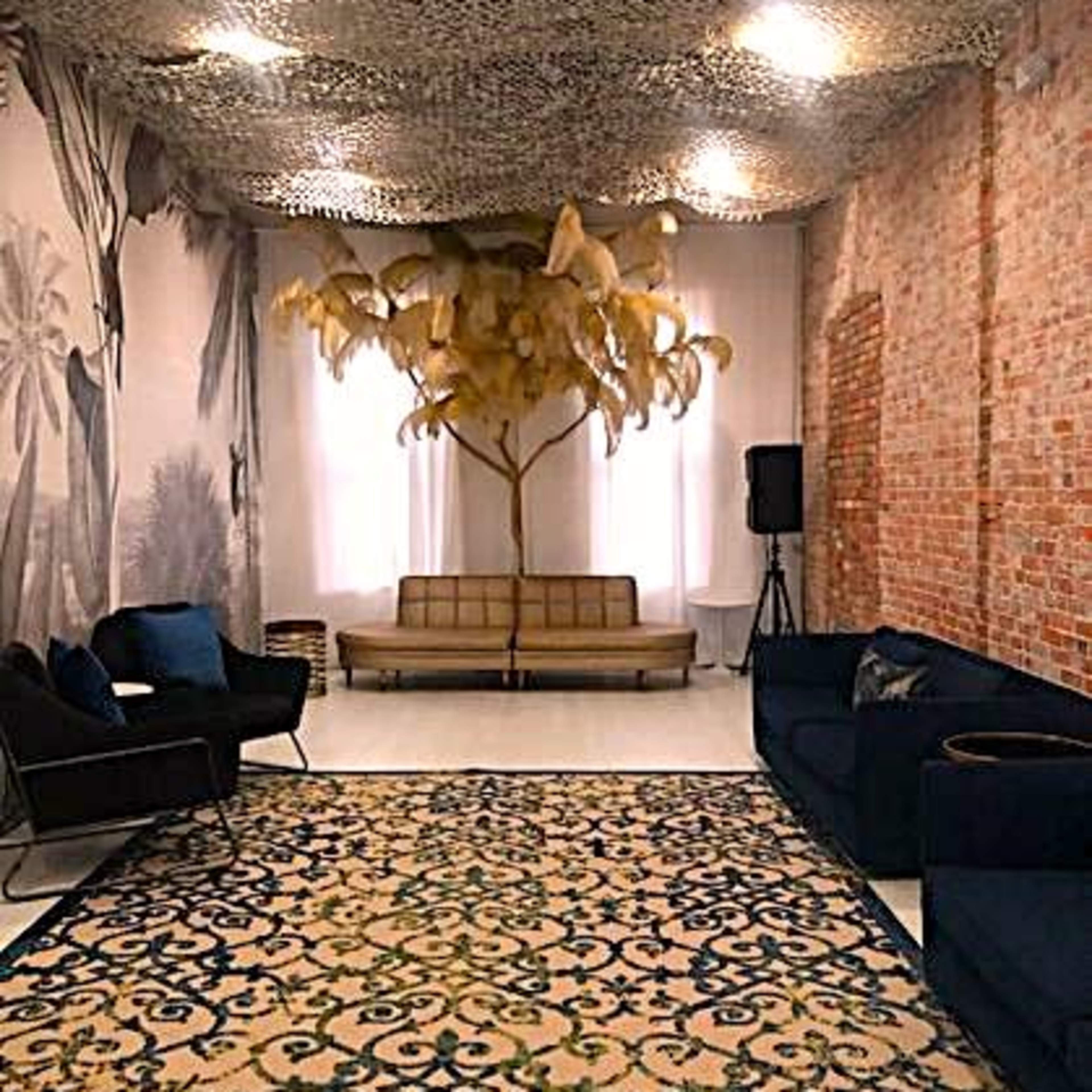 A stylish lounge area featuring a patterned rug, a vintage couch, and a decorative tree installation beneath a textured ceiling.