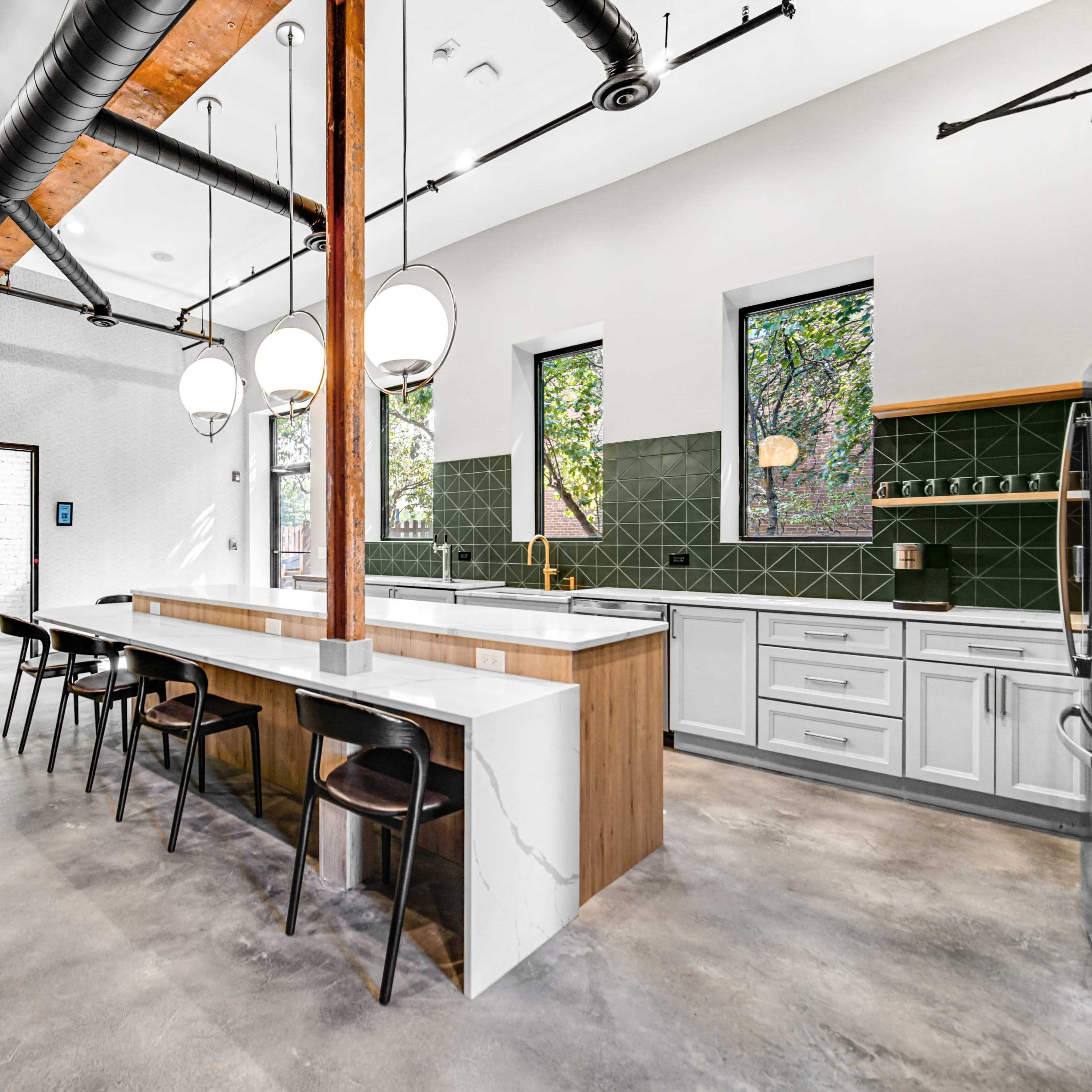 A modern kitchen with a central island, sleek cabinets, and large windows allowing natural light to enter.