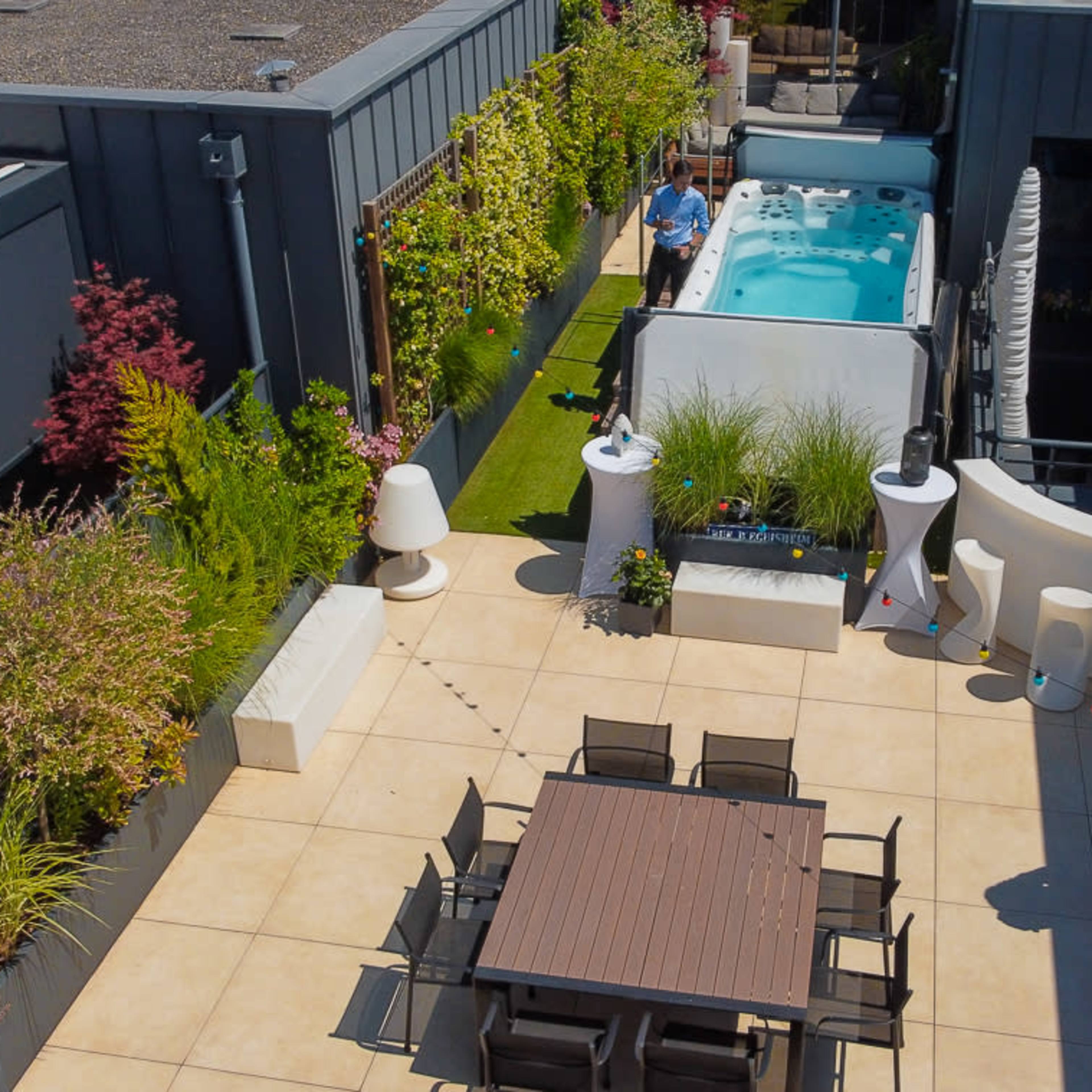 A spacious rooftop terrace with a hot tub, seating area, and landscaped greenery.