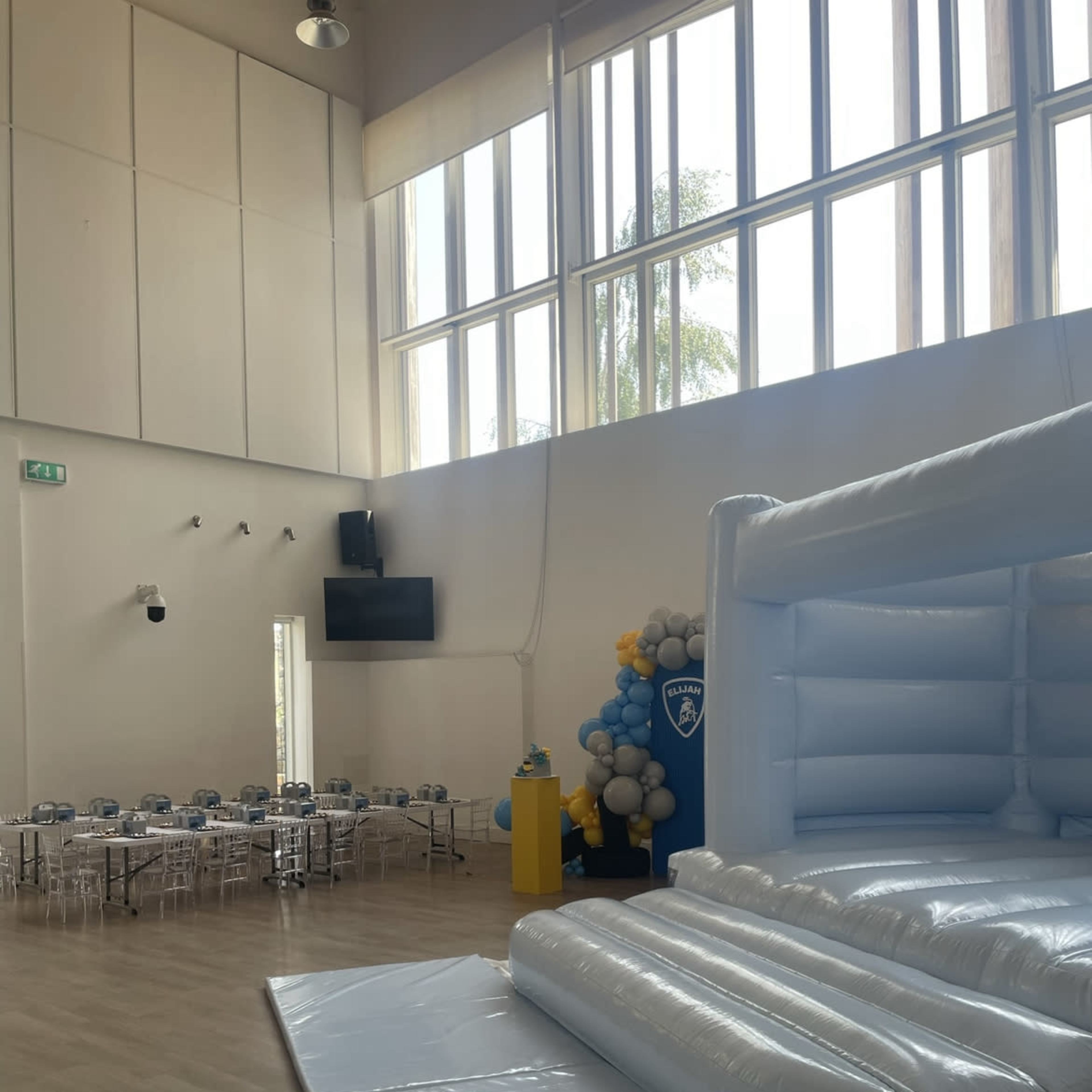 A brightly lit event space with a large inflatable bounce house on one side and a set of tables arranged for a gathering on the other.
