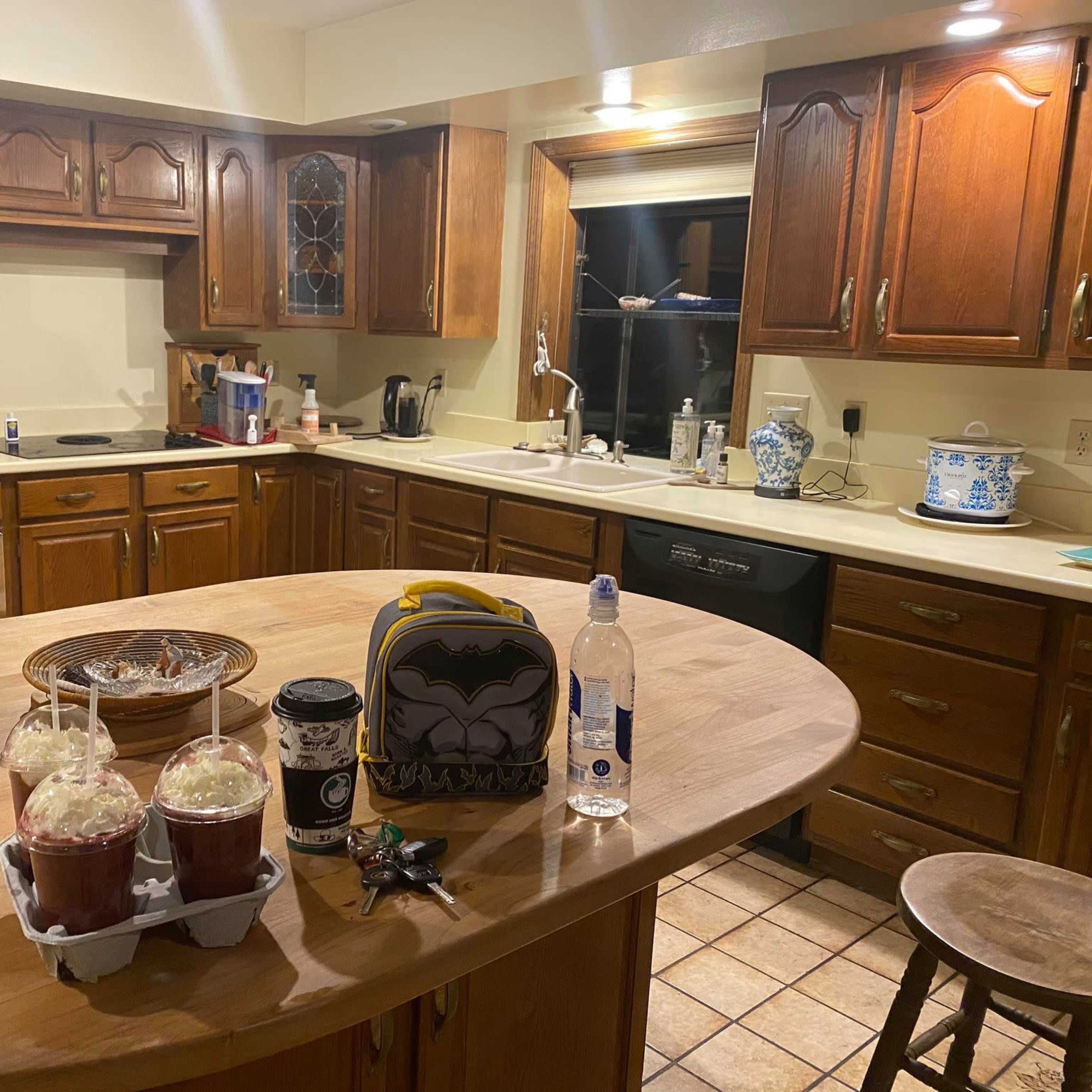The kitchen features wooden cabinets, a large island with two drinks topped with whipped cream, a backpack, a water bottle, and a coffee cup on the counter.