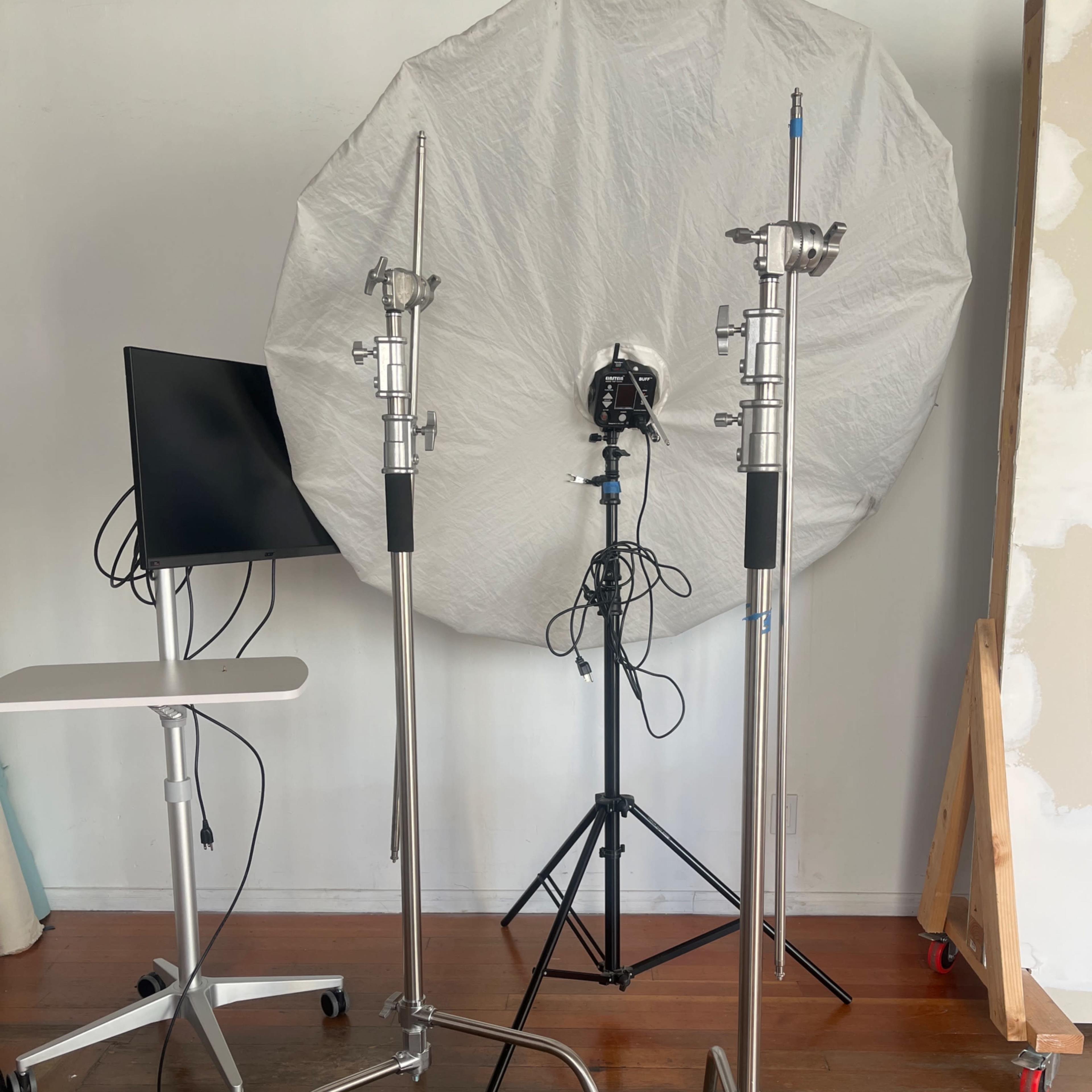 Two metal light stands beside a computer monitor and a large softbox positioned on a tripod.