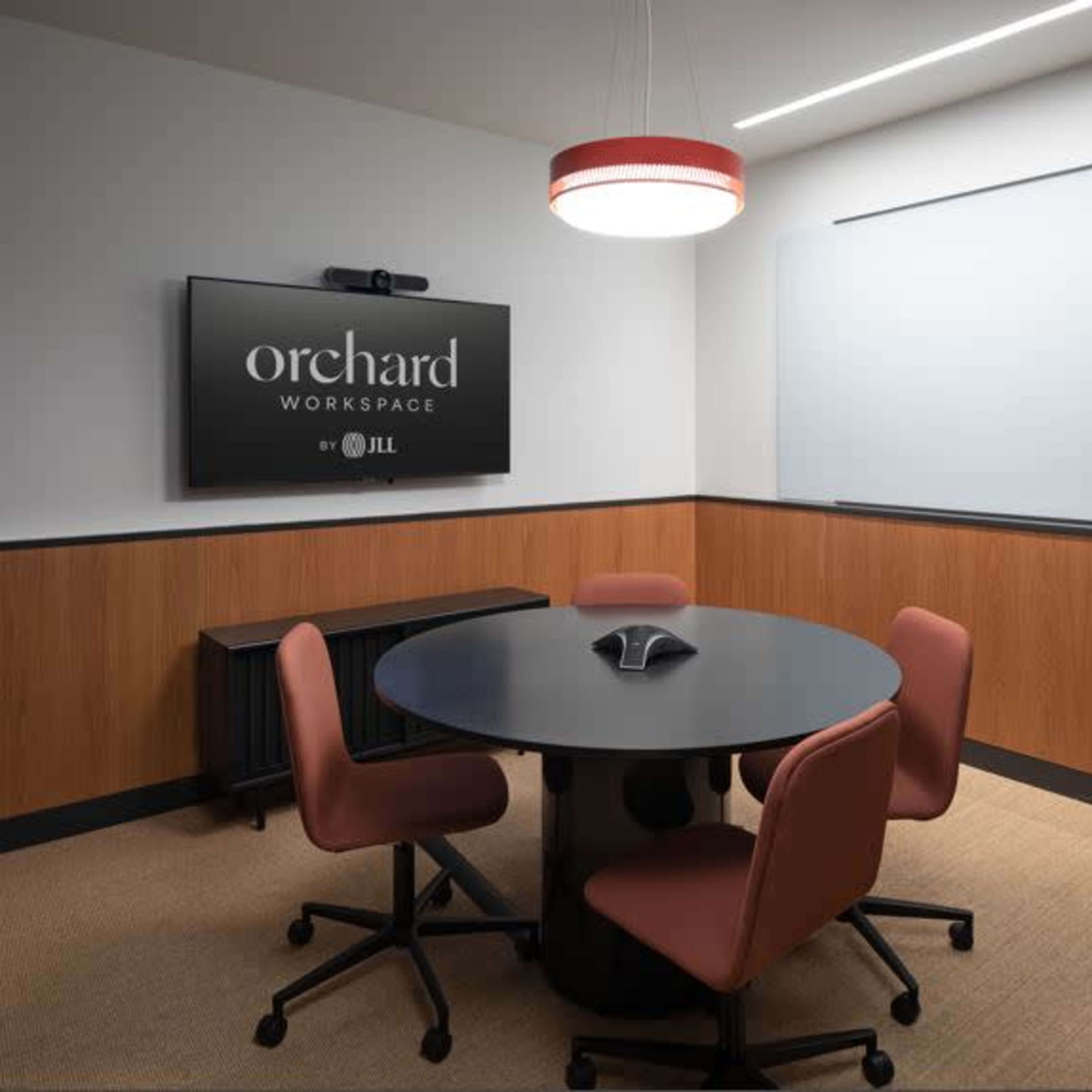 A modern conference room features a round black table surrounded by four brown chairs, with a television and whiteboard on the walls.