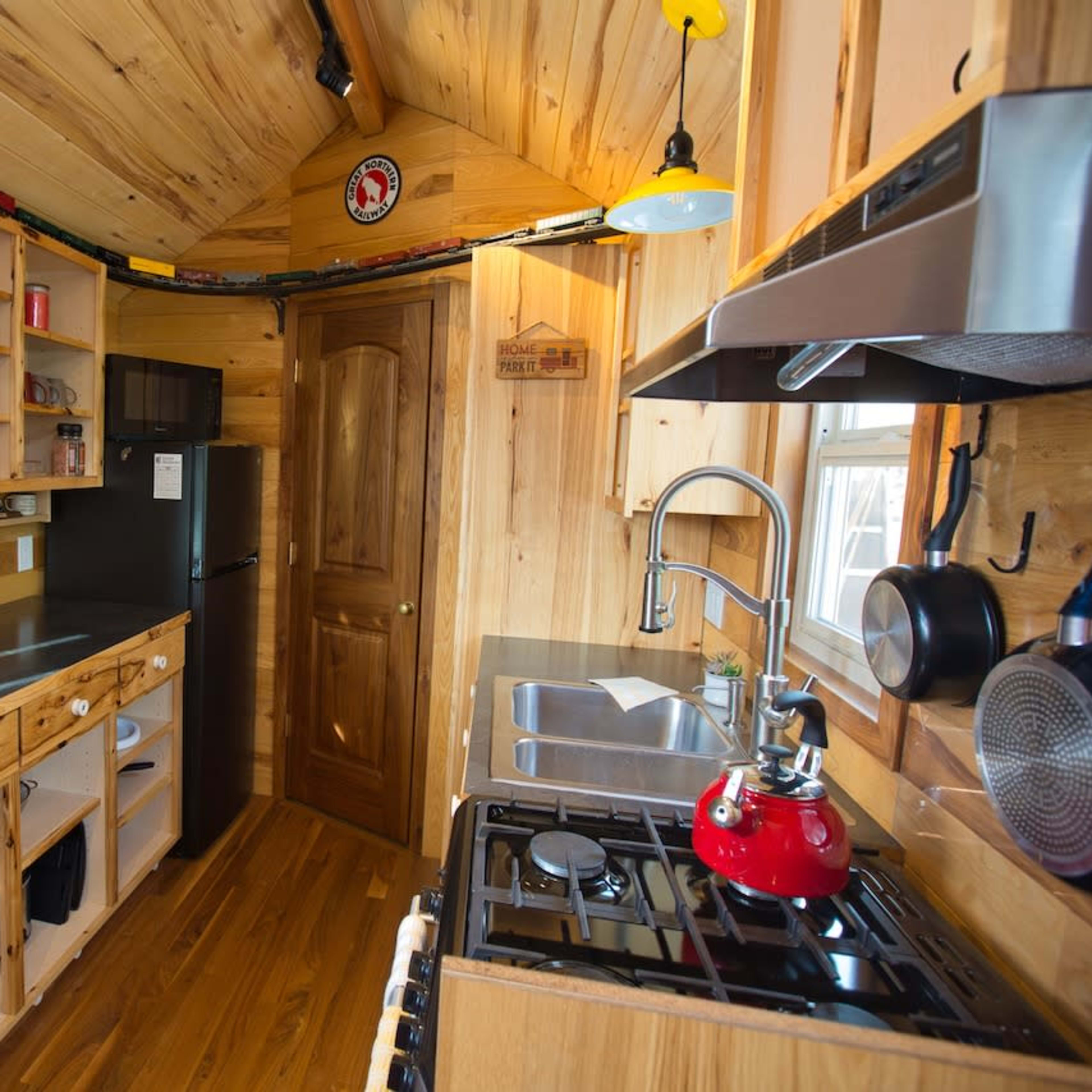 A small, well-organized kitchen with wooden cabinets, a stainless-steel sink, a gas stove, and a refrigerator.