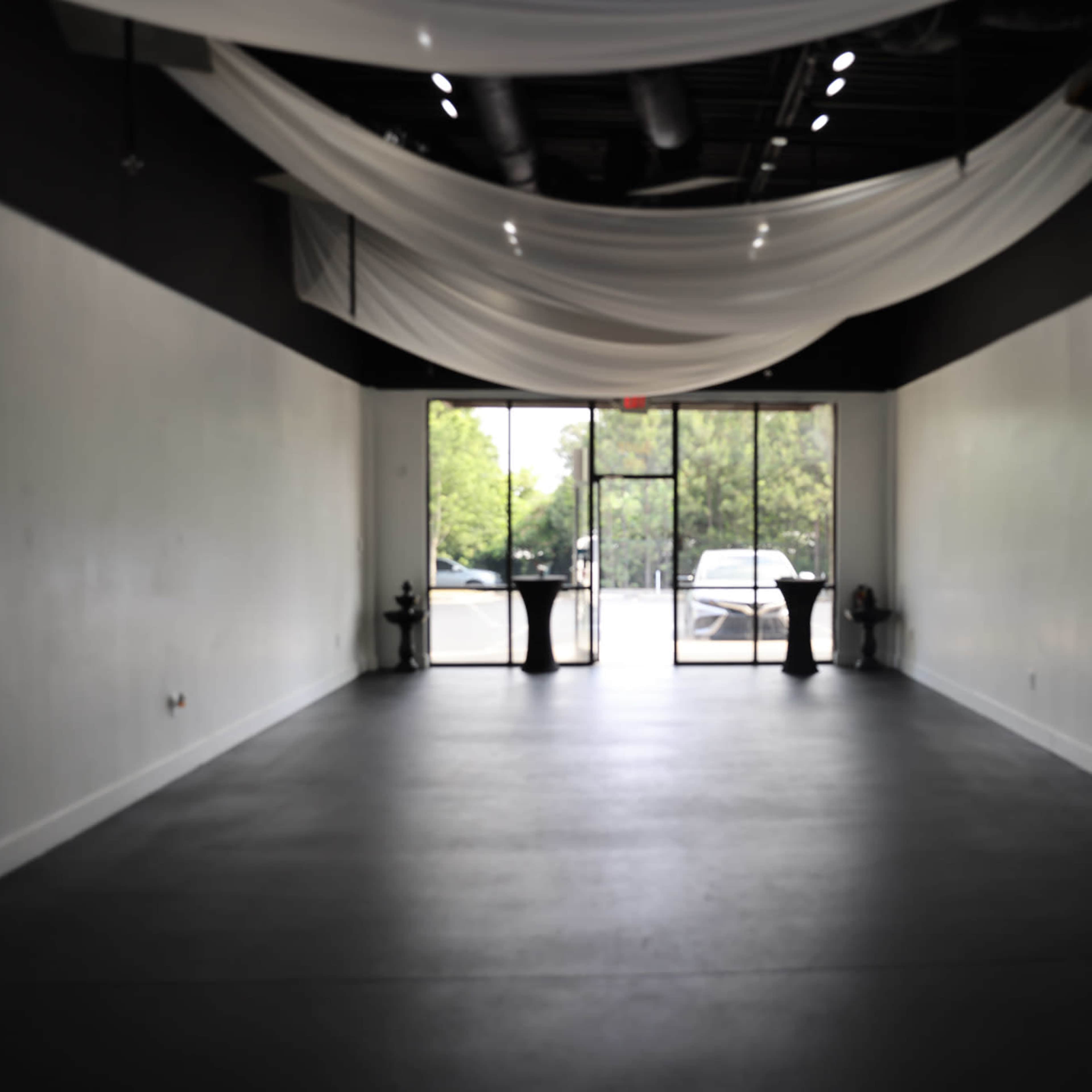 An empty interior space features a large glass entrance surrounded by draped fabric on the ceiling.