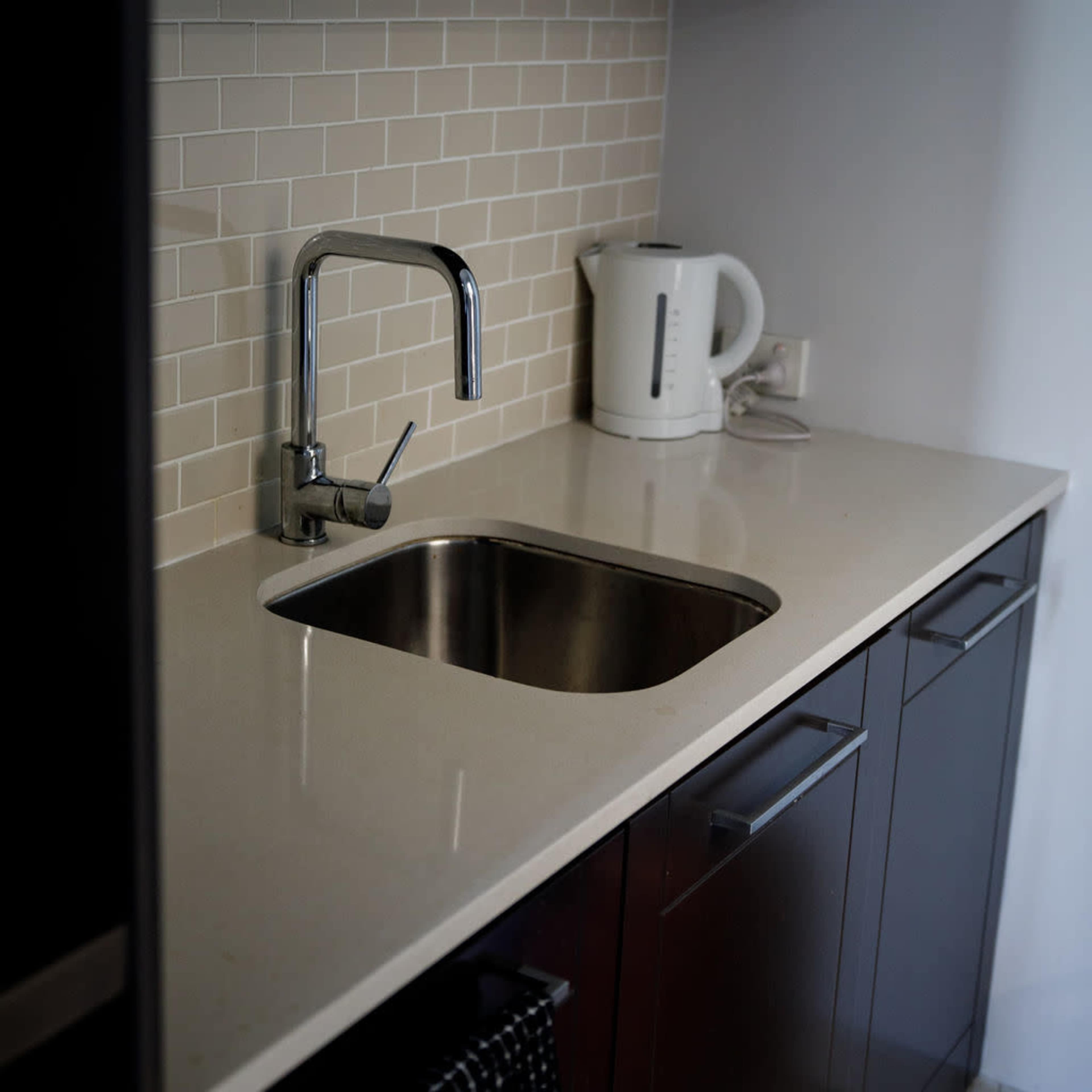 A modern kitchen sink area with a stainless steel faucet, a kettle, and a clean countertop.