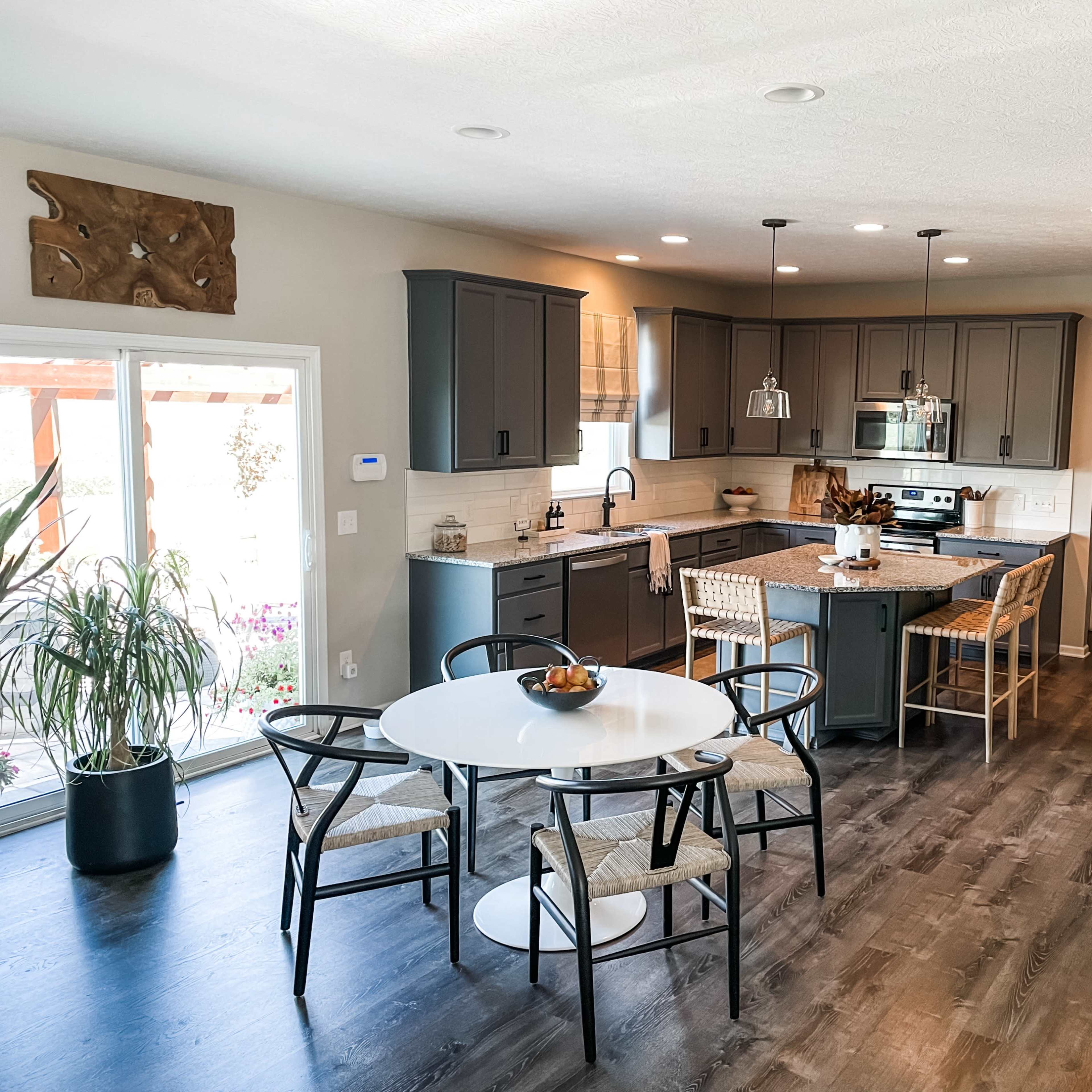 A modern kitchen and dining area feature gray cabinetry, a central island with bar seating, and a round dining table surrounded by chairs.