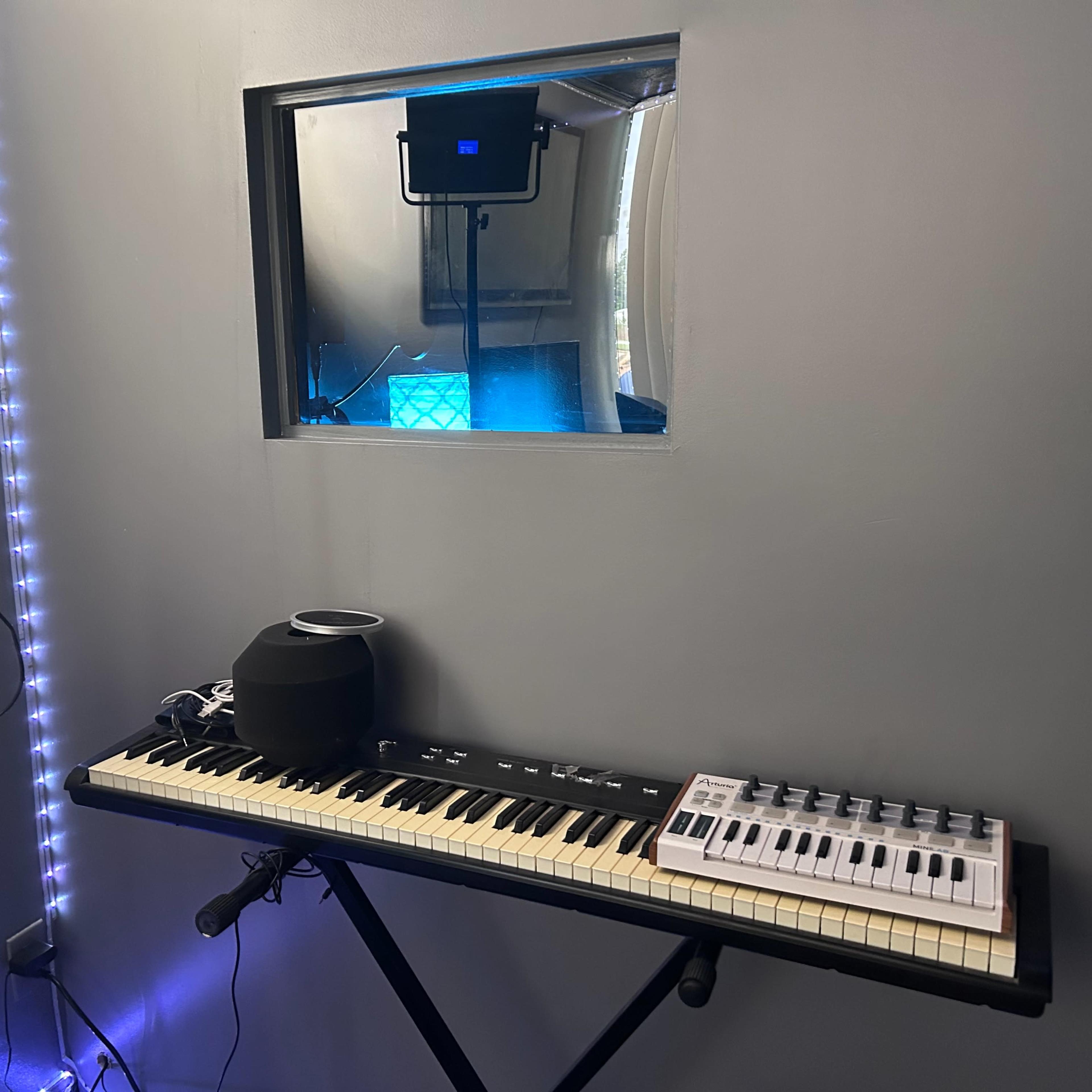 A keyboard and a small speaker are positioned in front of a window looking into a room illuminated with blue light.