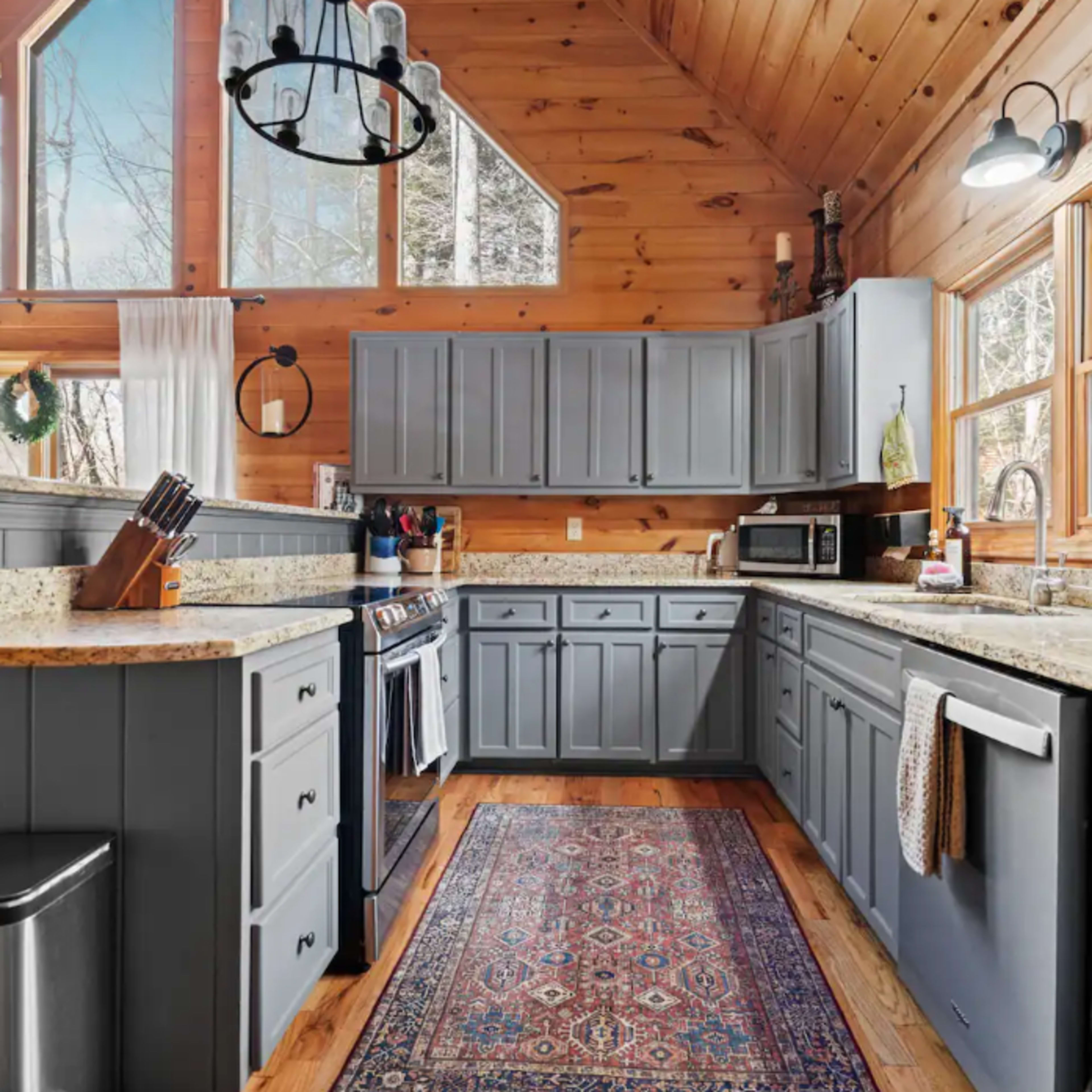 A spacious kitchen with gray cabinets, granite countertops, and large windows that offer a view of the outdoors.