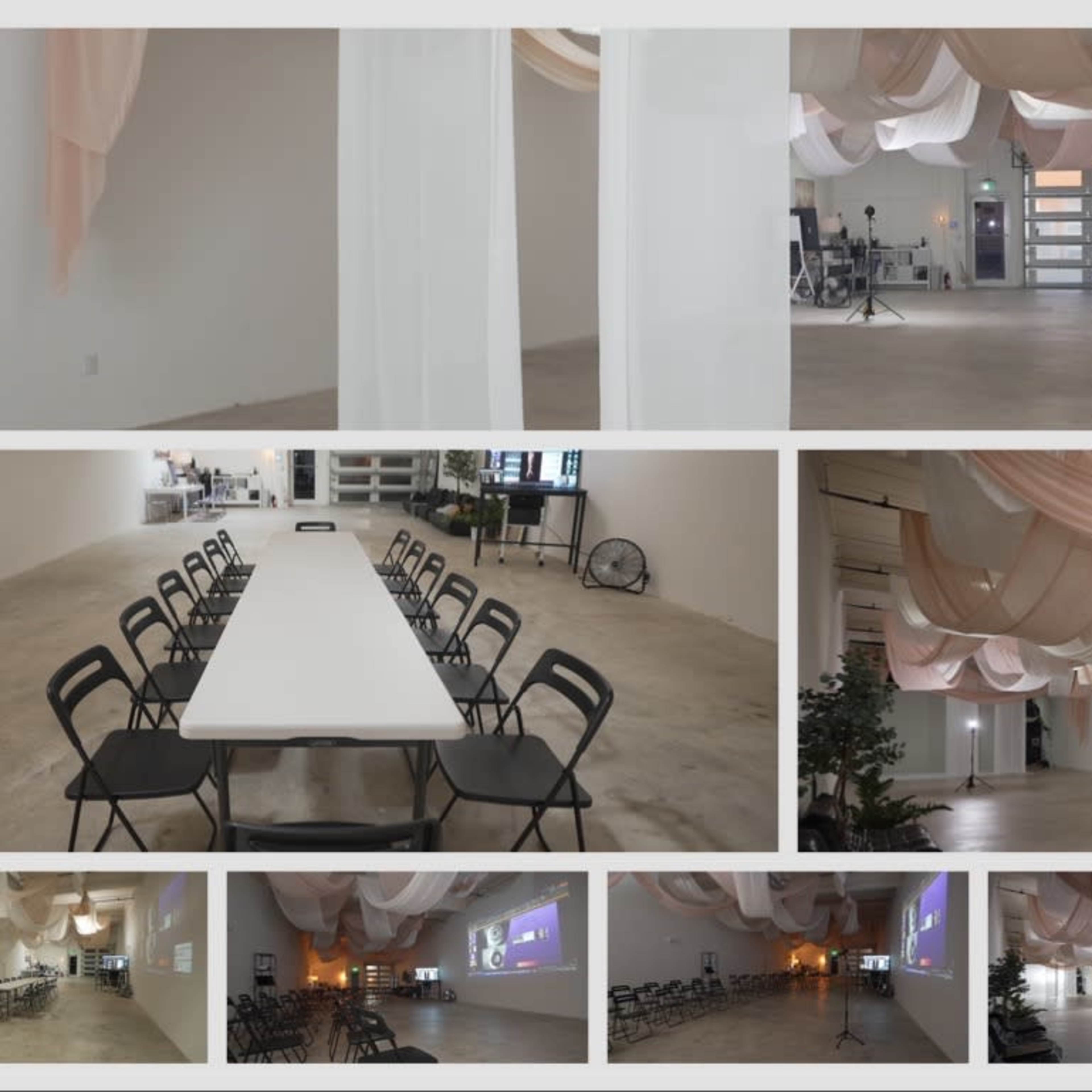 A spacious, minimally decorated indoor venue with a long table set for a meeting, surrounded by soft fabric drapes hanging from the ceiling.