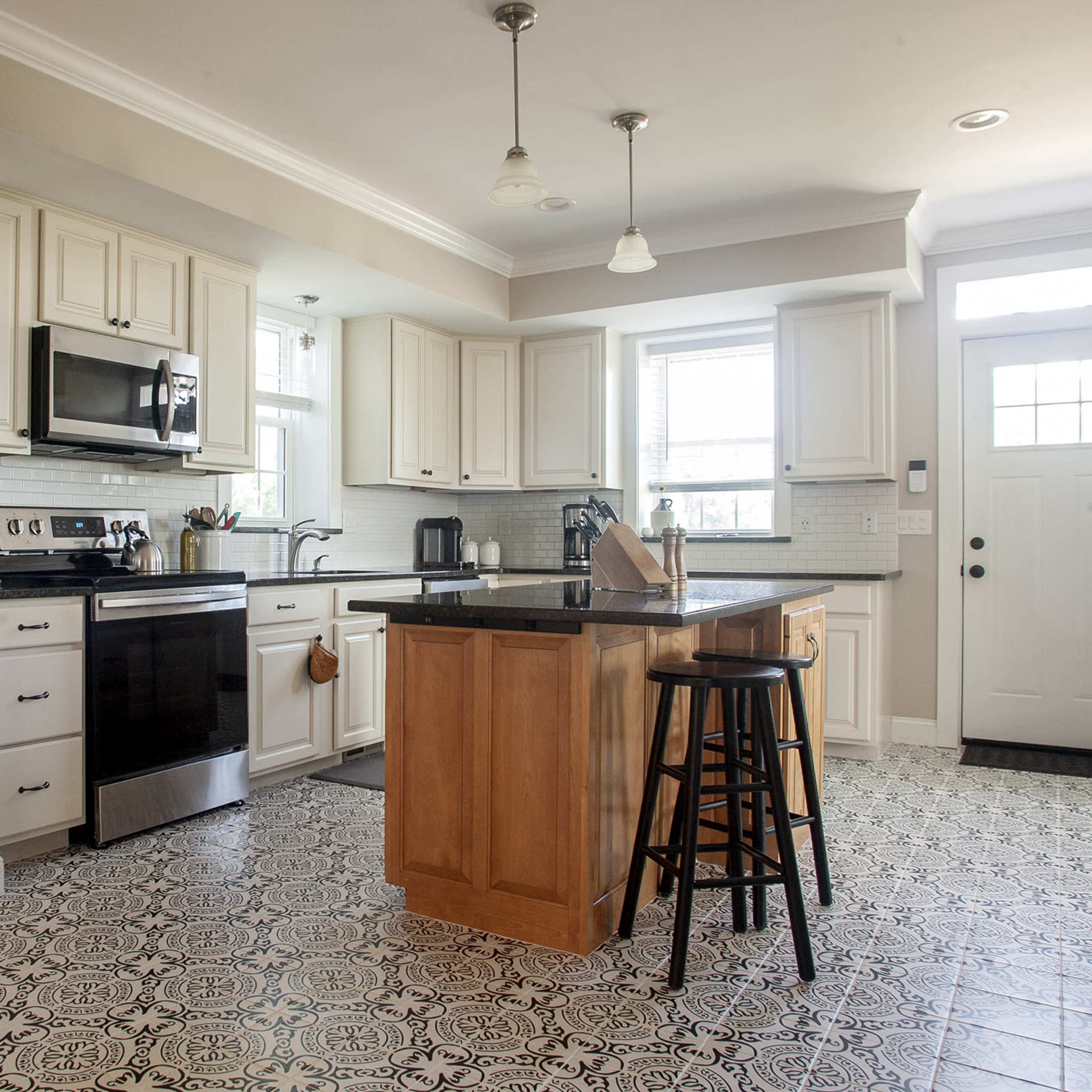 A modern kitchen with stainless steel appliances, white cabinetry, a central island with wooden countertop, and patterned black and white tiles on the floor.