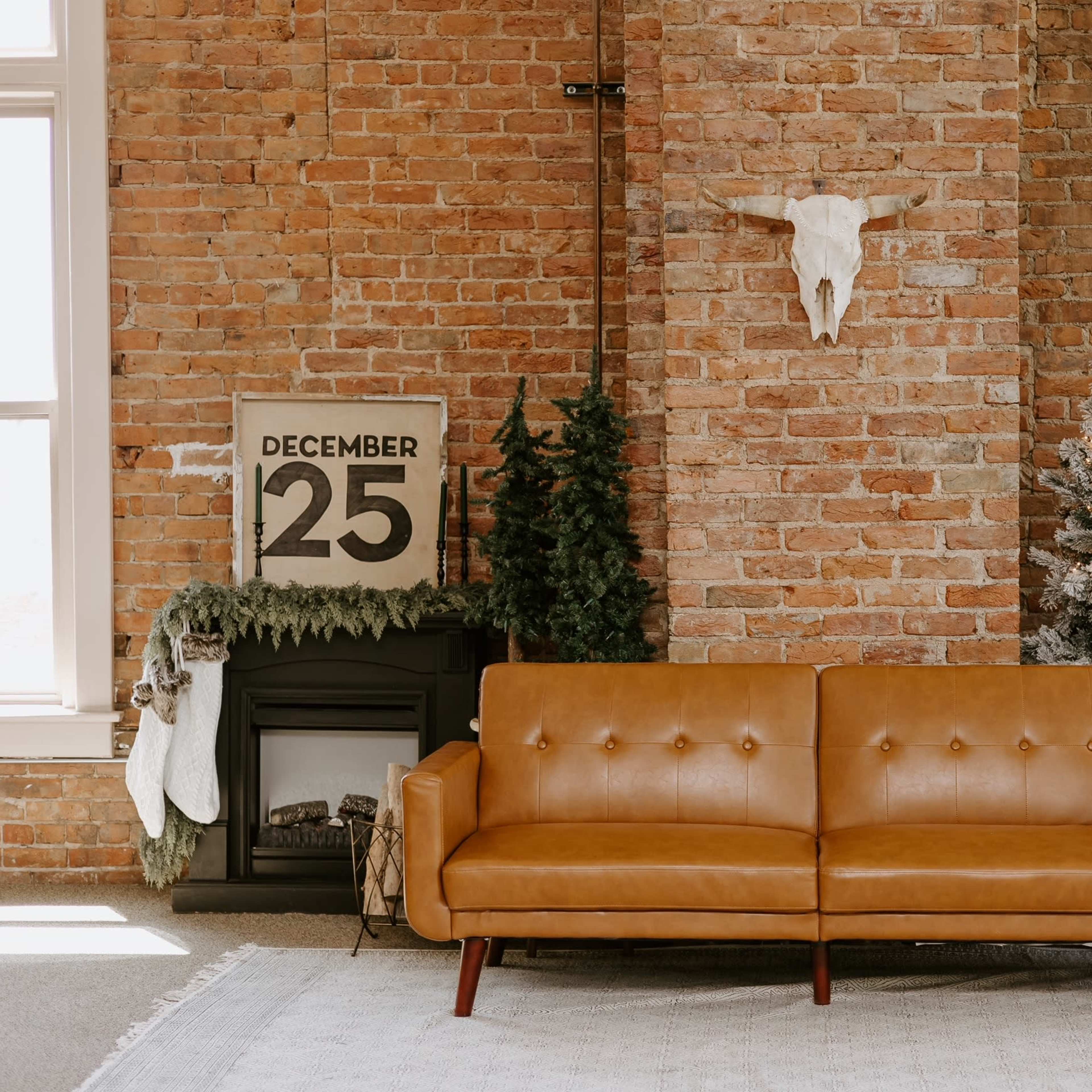 A brown leather sofa in front of a brick wall, with a decorated Christmas tree, a fireplace, and a sign displaying "DECEMBER 25" nearby.