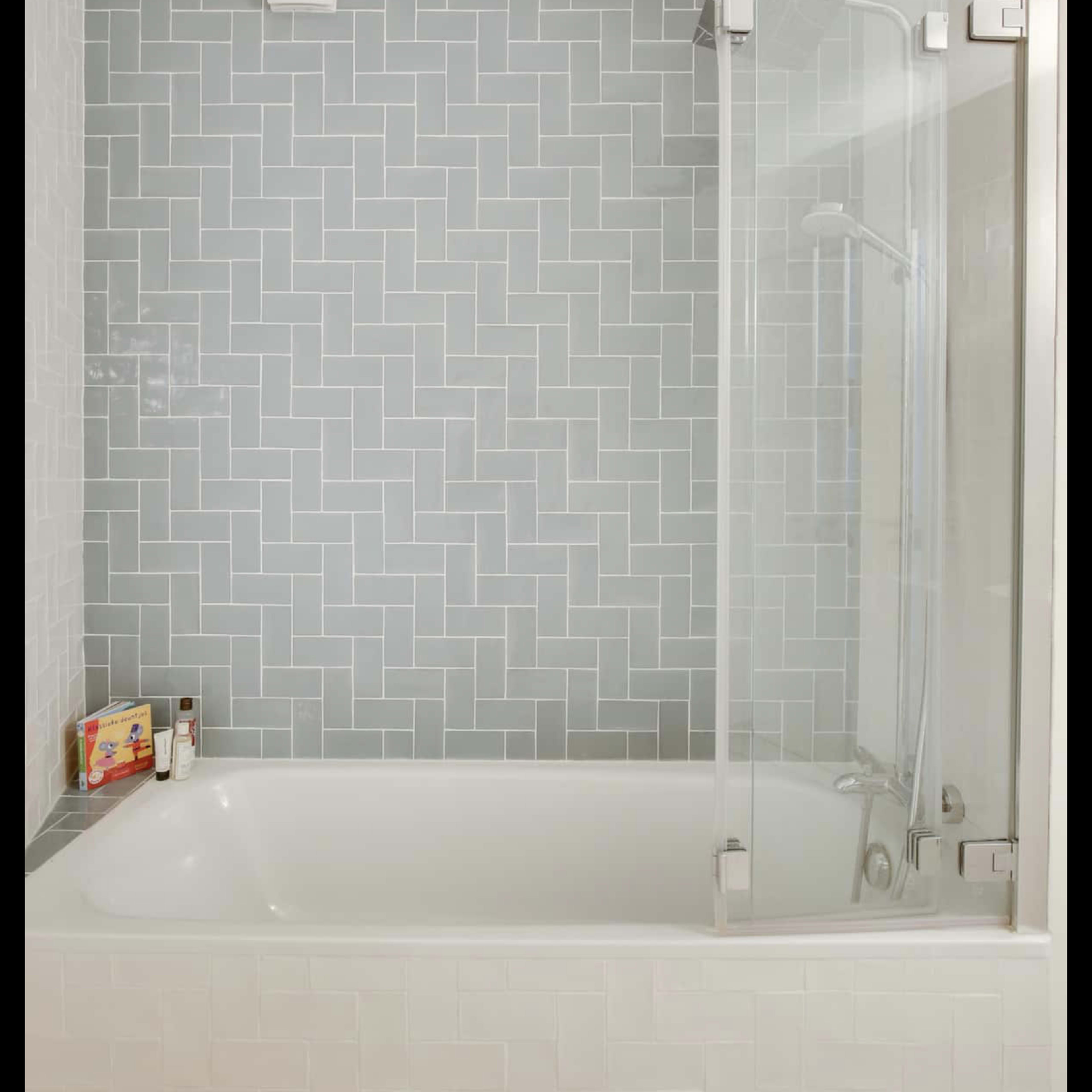 A modern bathroom with a glass shower enclosure next to a rectangular bathtub and a tiled wall featuring a light gray, brick-patterned design.
