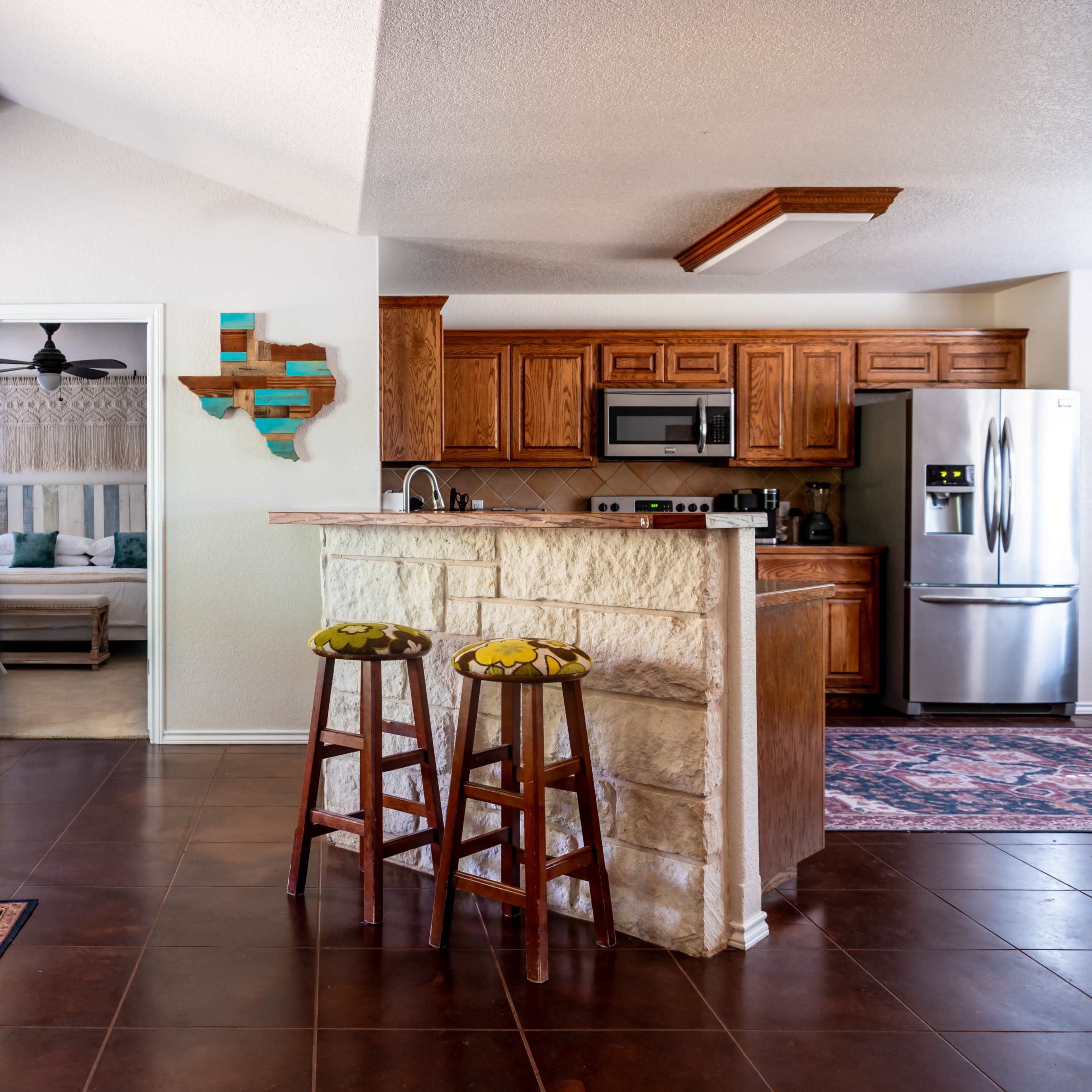 A spacious open-concept living area with a kitchen, featuring wooden cabinetry, a stone bar, and seating areas along with decorative wall art.