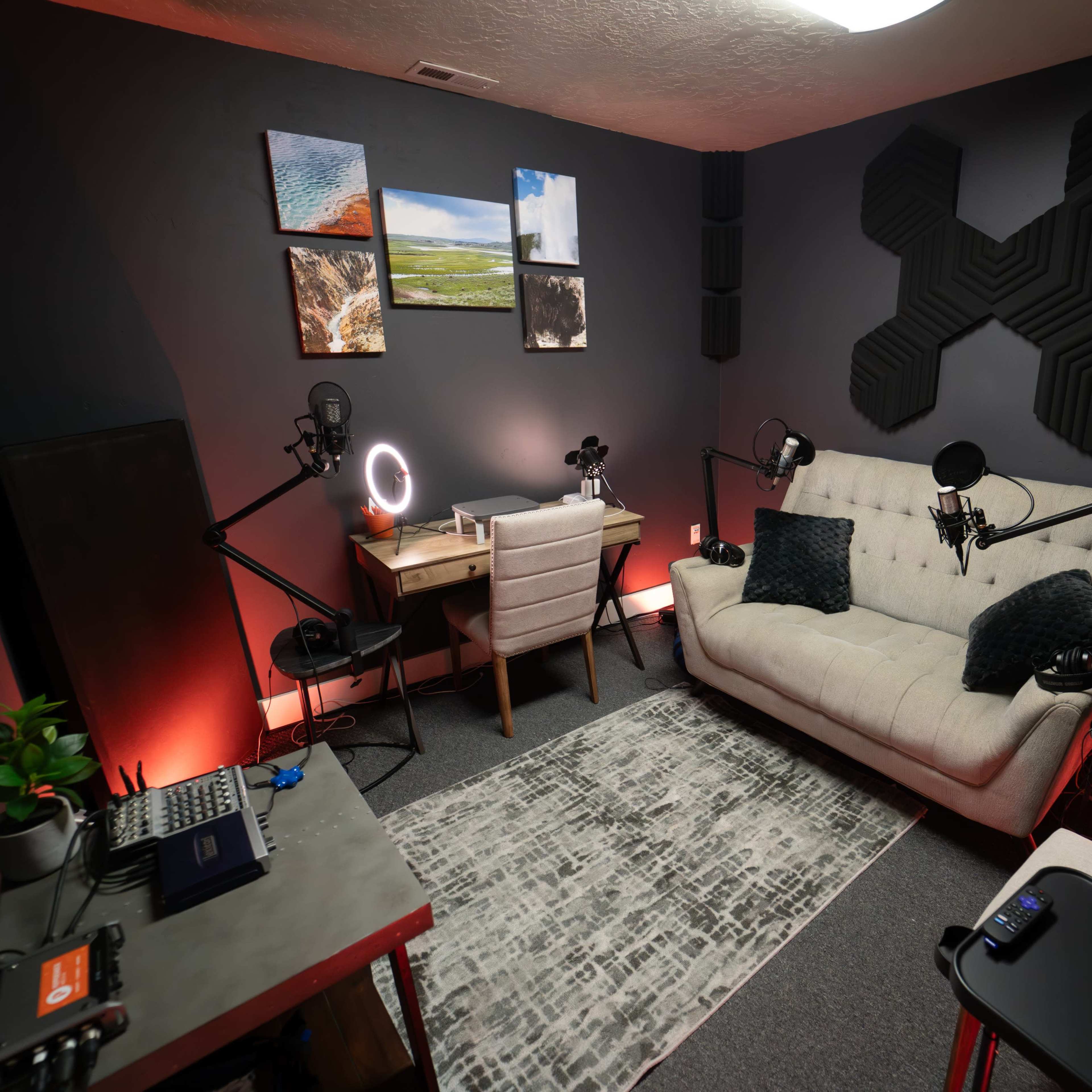 A modern recording studio features a sofa, desk with microphones, and wall-mounted acoustic panels, illuminated by soft lighting.