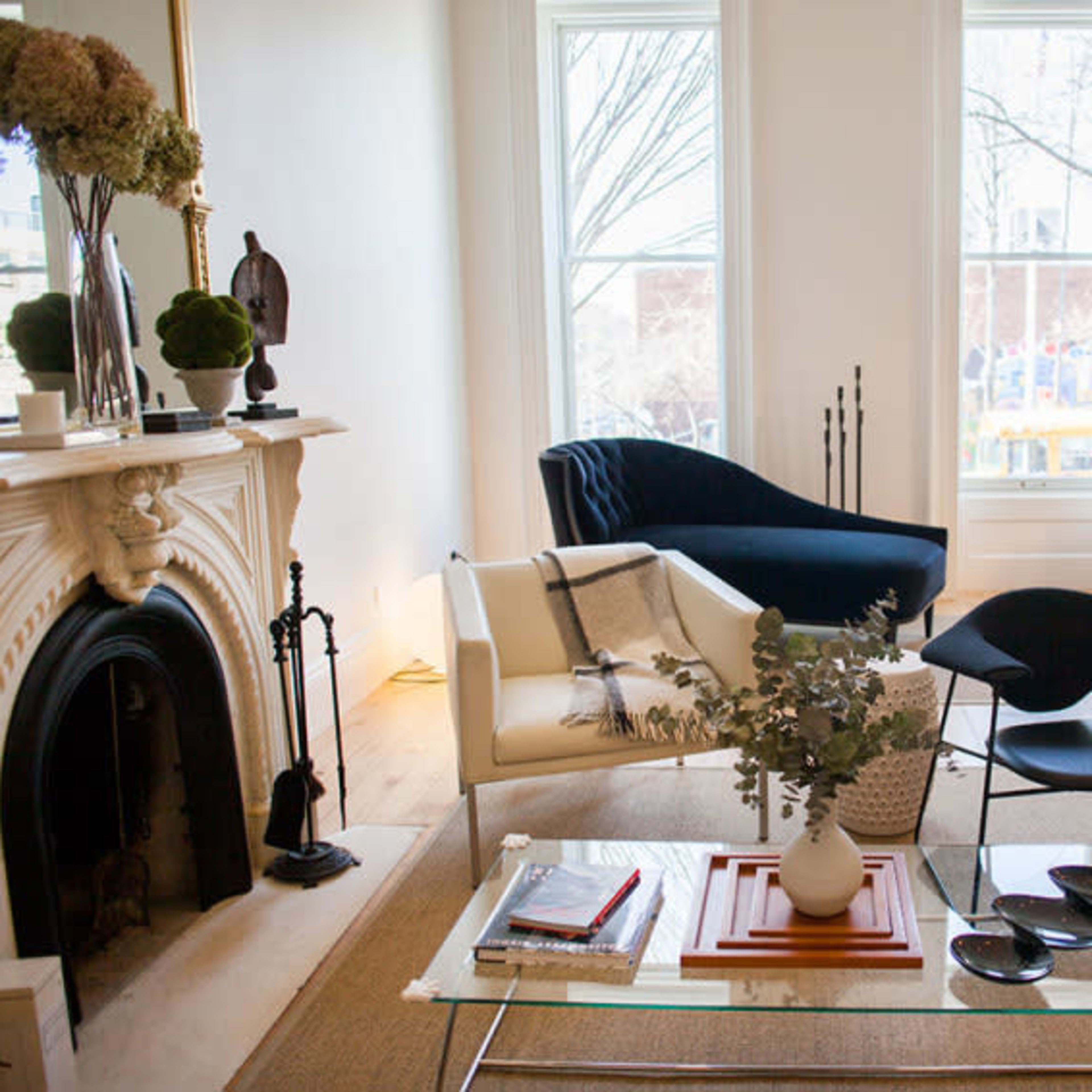 A living room with a fireplace, a white sofa, a blue chair, a glass coffee table, and a wooden piano.
