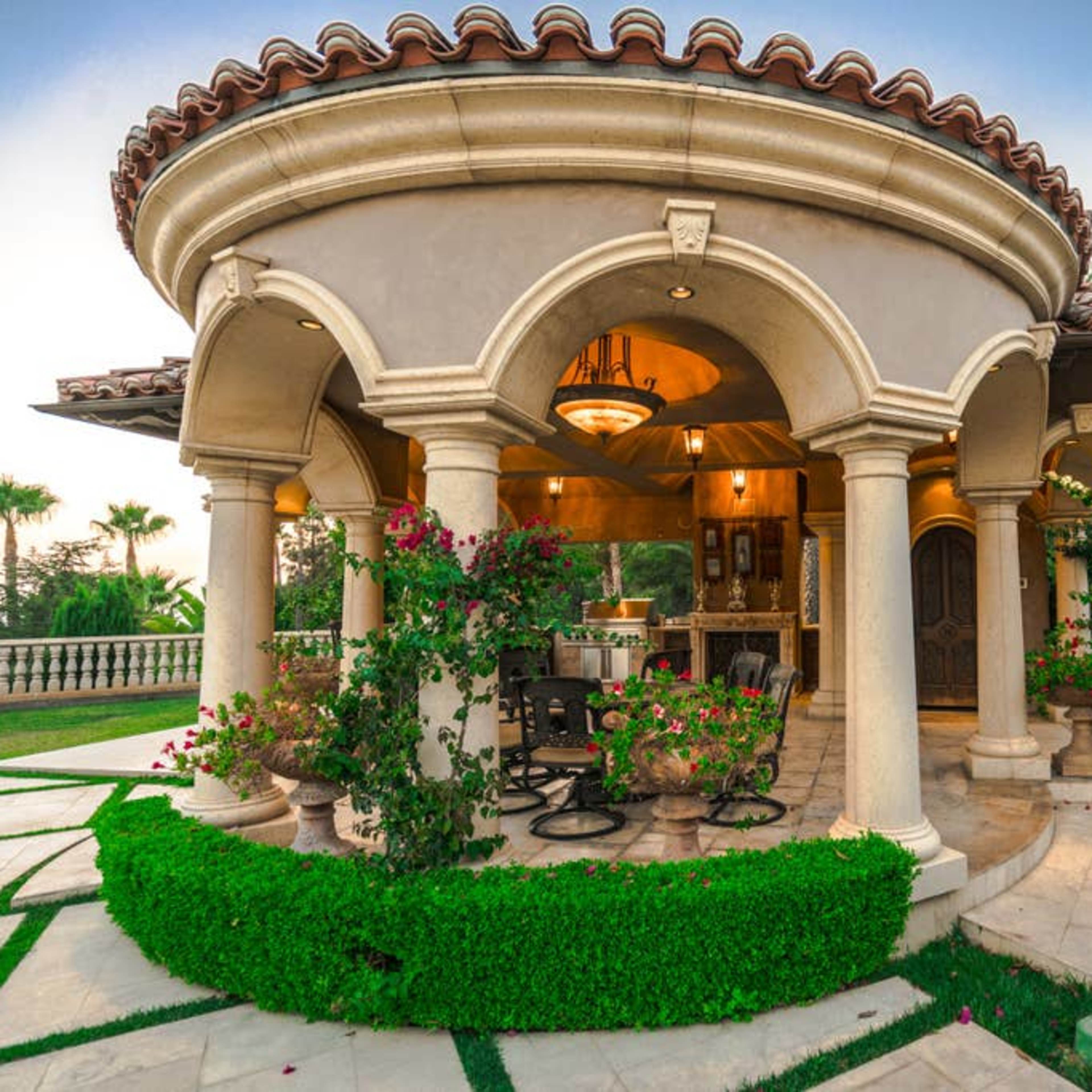 A beautifully designed round patio with columns, decorated with potted plants and flowers, adjacent to a landscaped lawn.