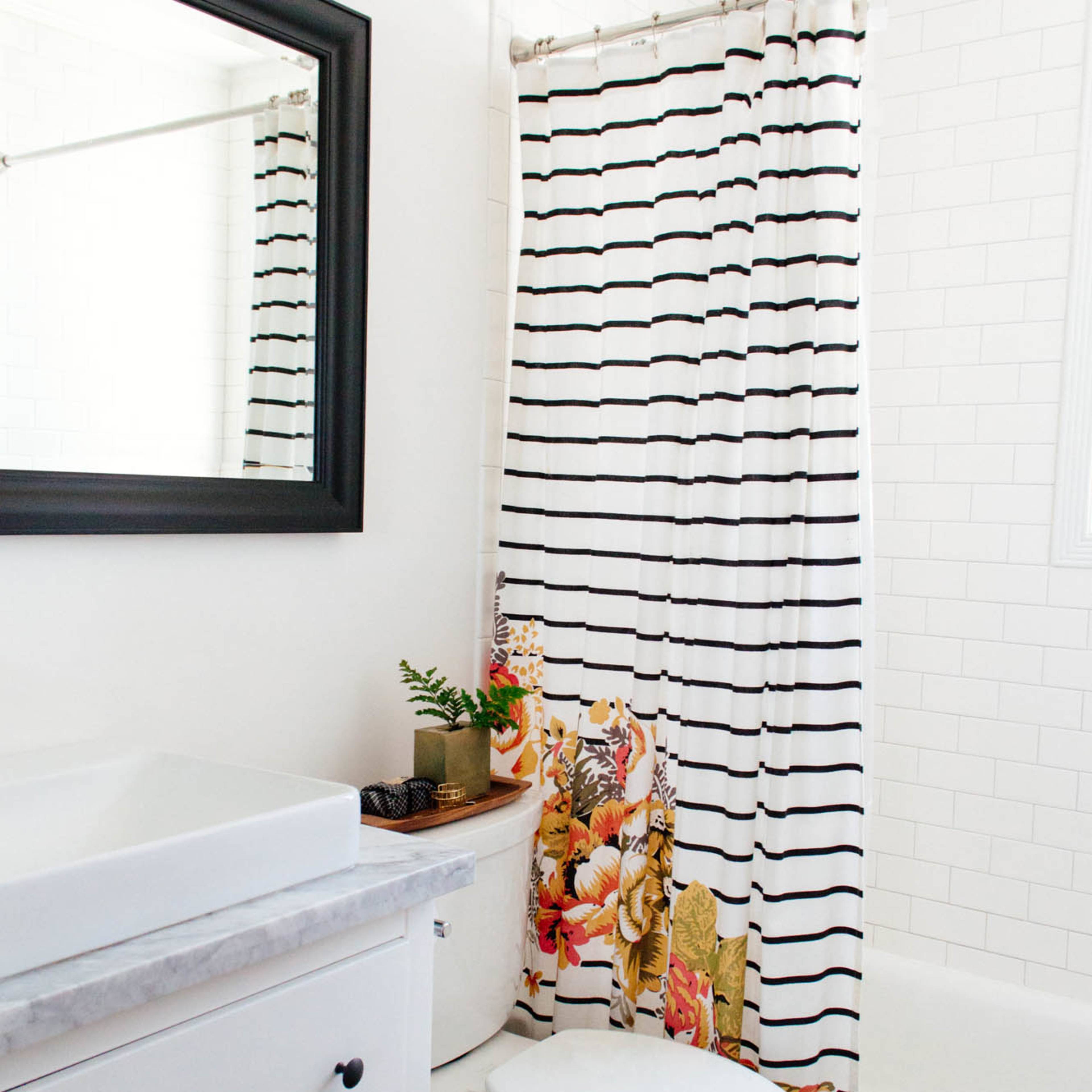 A bathroom with a white tiled wall, a black framed mirror, a striped shower curtain, and a toilet next to a sink with a marble countertop.